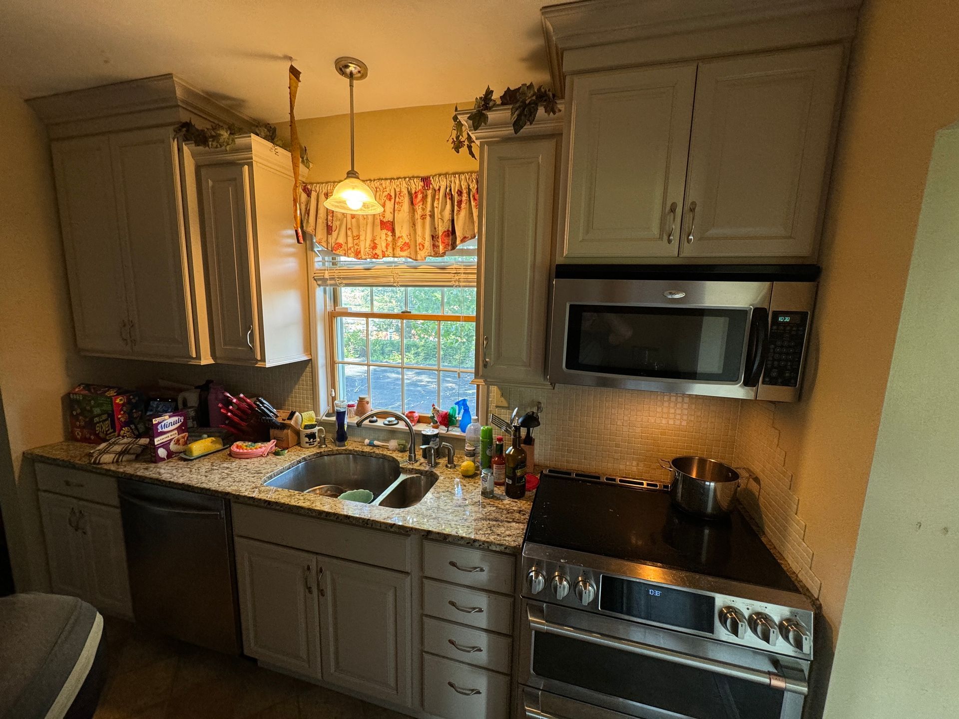 Kitchen with light gray cabinets, stainless steel appliances, and a window above the sink.