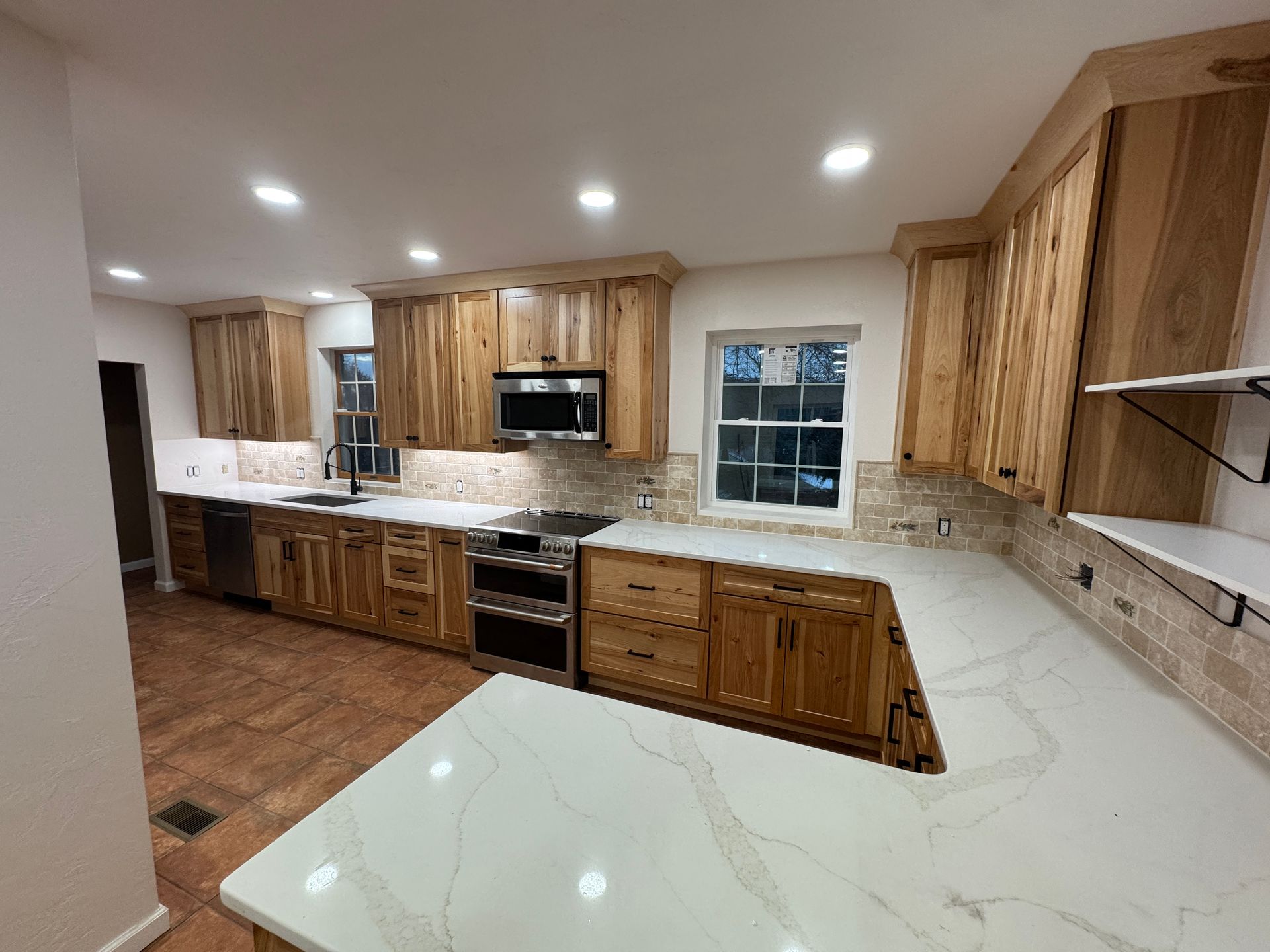 Kitchen with light wood cabinets, white countertops, and brick-style backsplash. Island and overhead lighting.