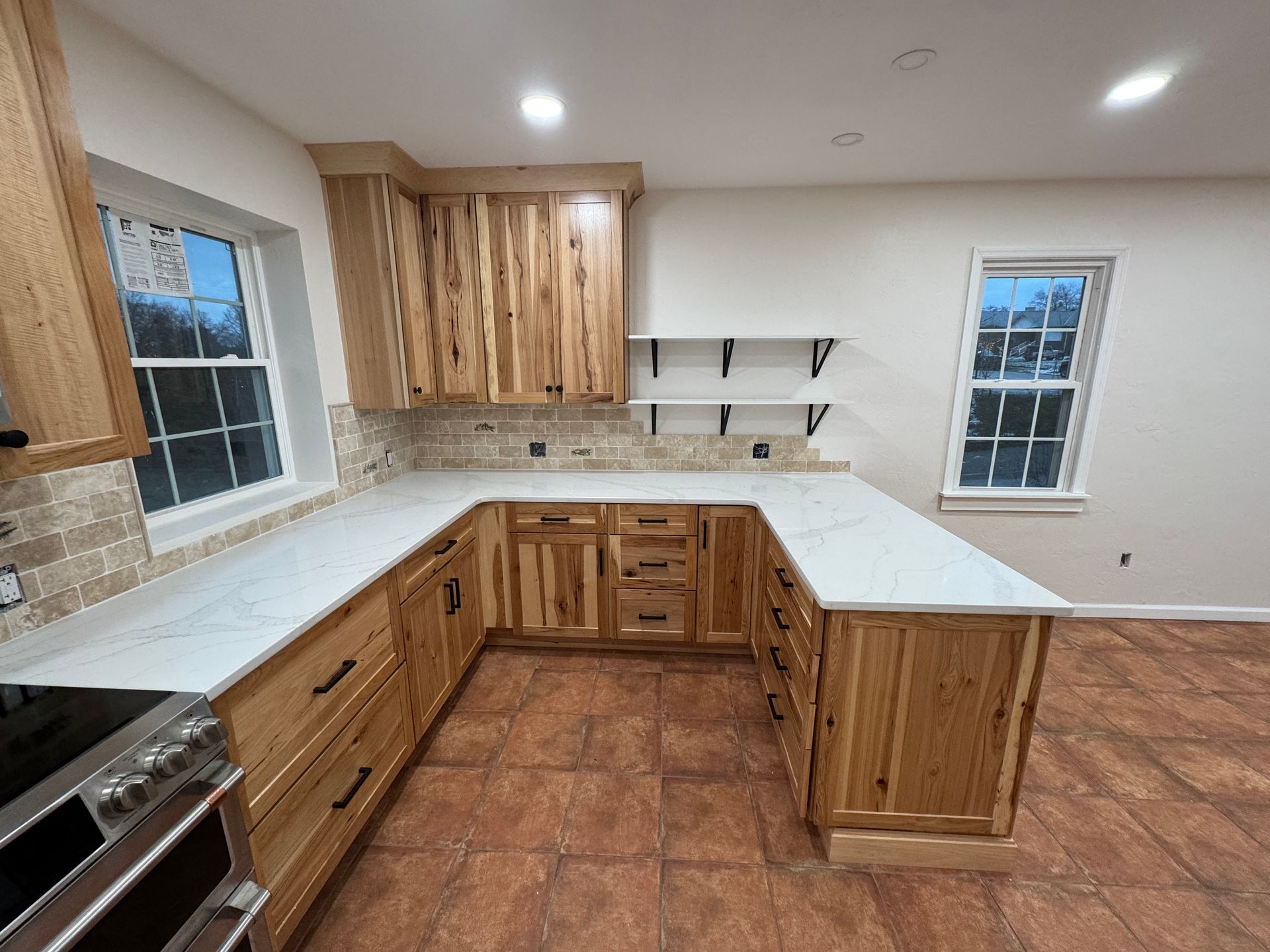 U-shaped kitchen with light wood cabinets, white countertops, and brick tile backsplash.