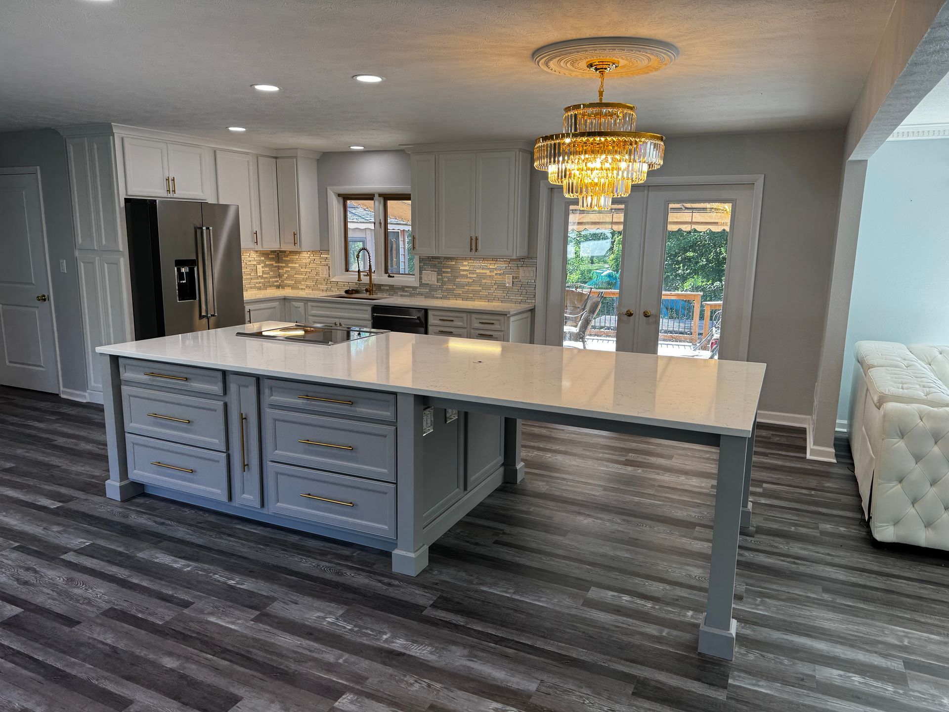Gray and white kitchen with island, cabinets, quartz counters, chandelier, and gray wood-look flooring.