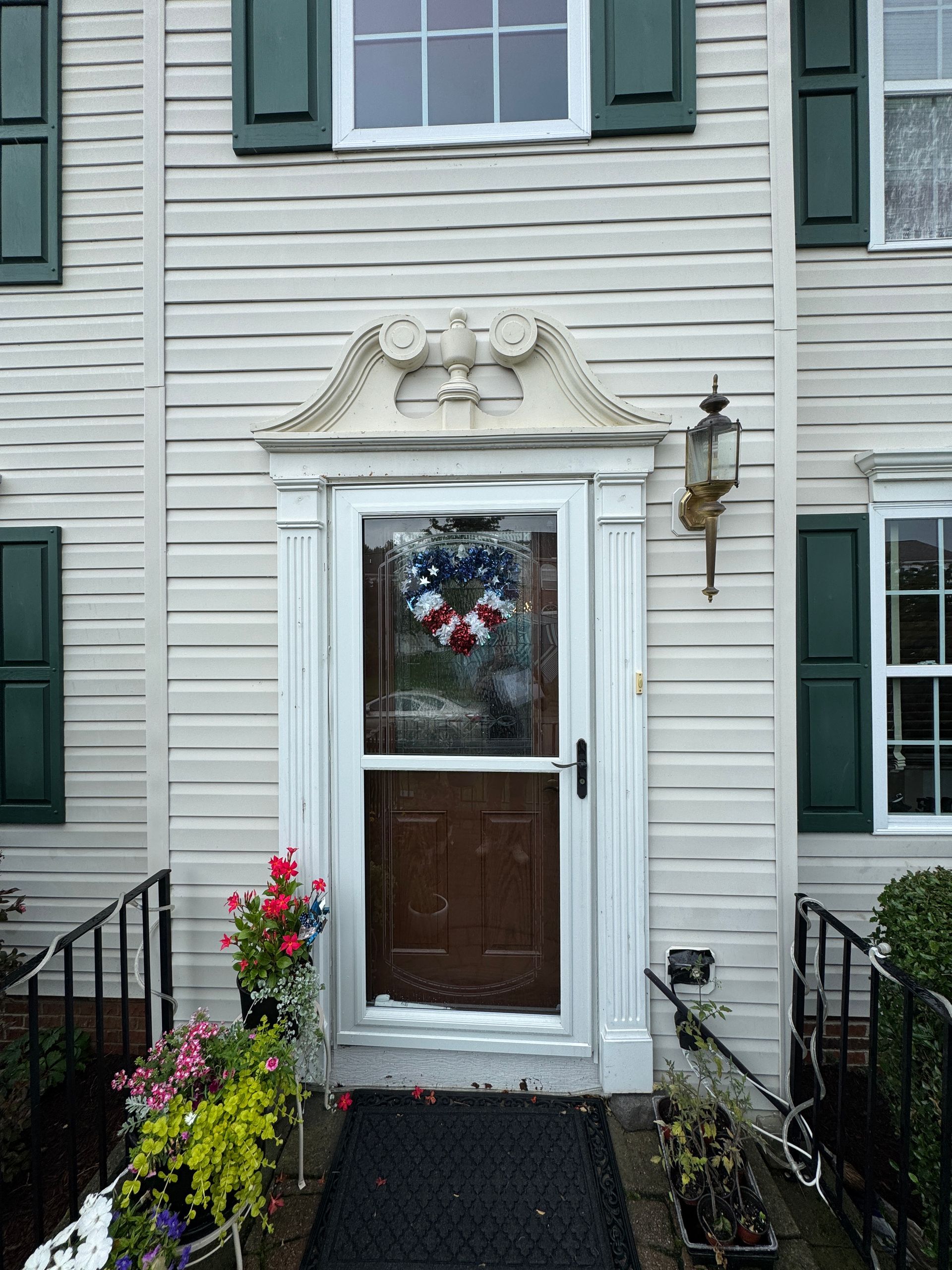 Front door of a house with cream siding, a decorative pediment, and a patriotic wreath.