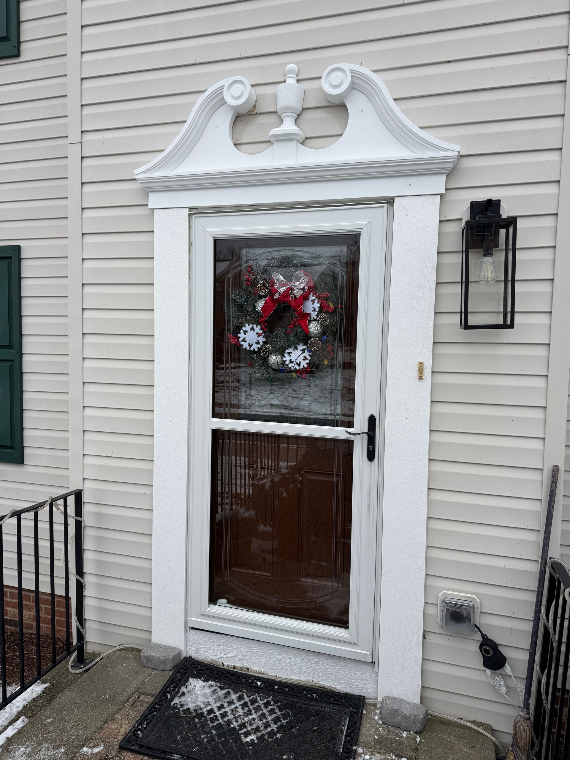 White doorway with ornate trim, wreath, and black lantern on a light-colored building.