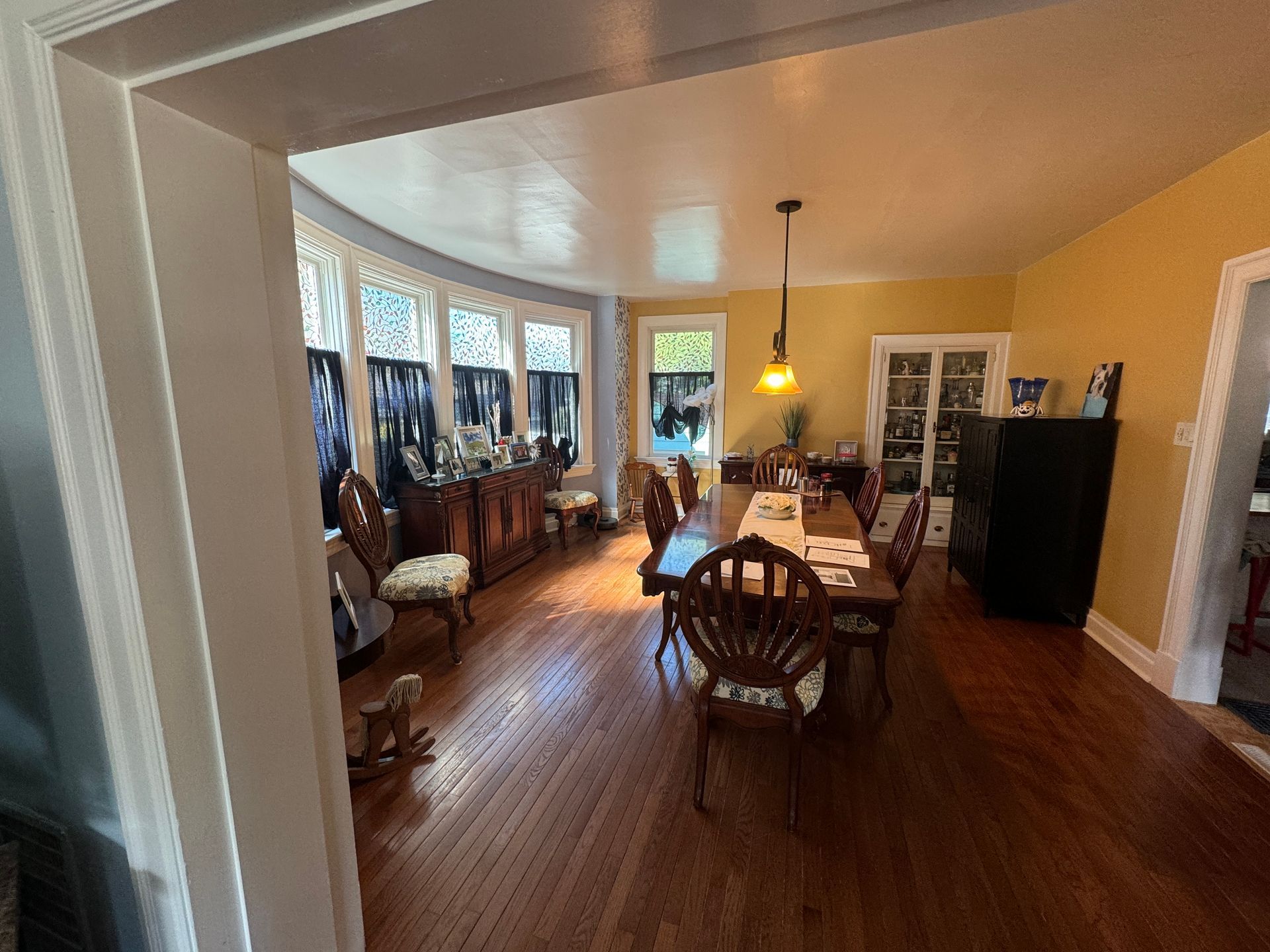 Dining room with hardwood floors, a long table, and a curved bay window. Yellow walls.