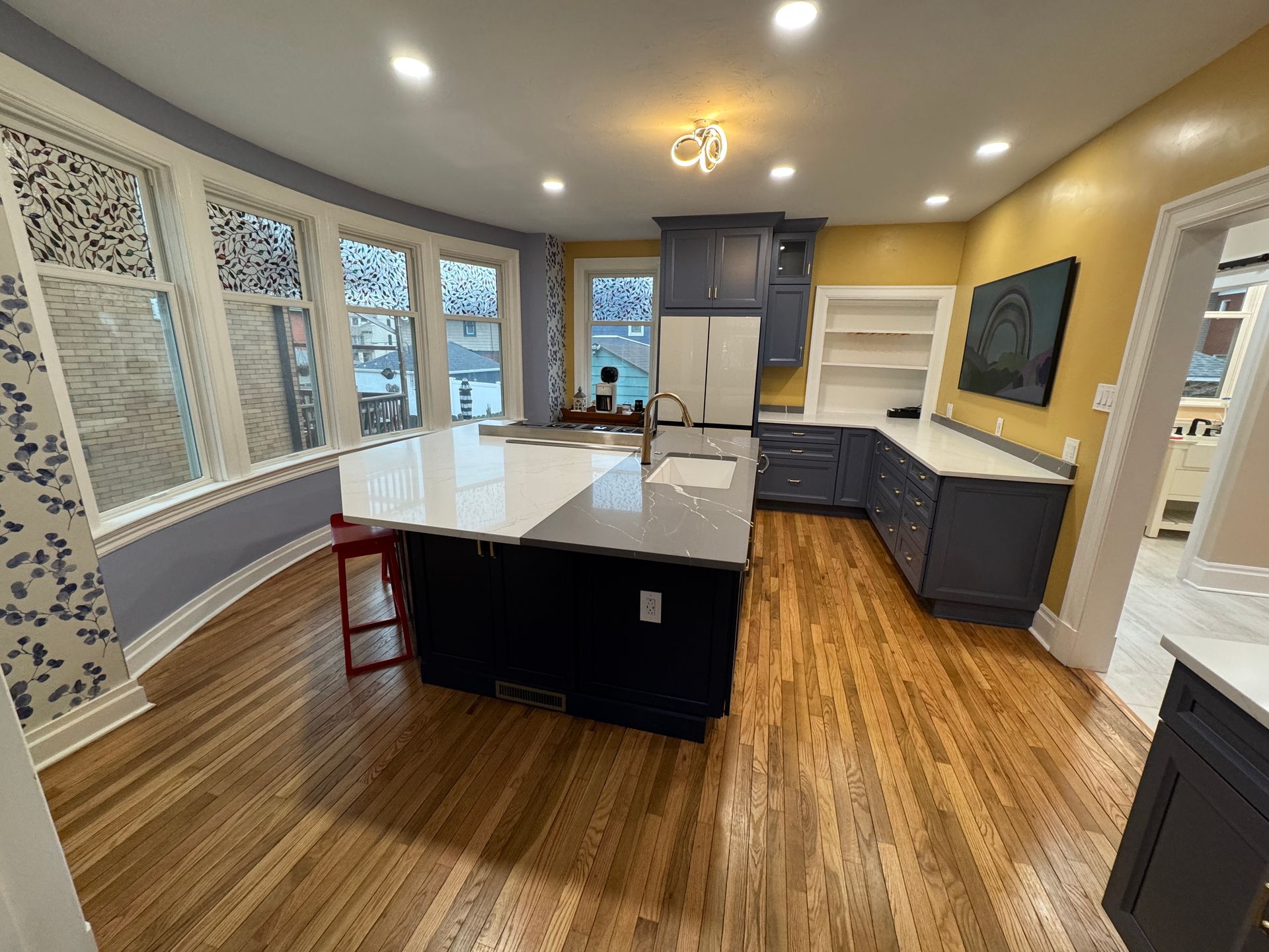 Spacious kitchen with a large island, blue cabinets, wooden floor, and yellow and blue walls.