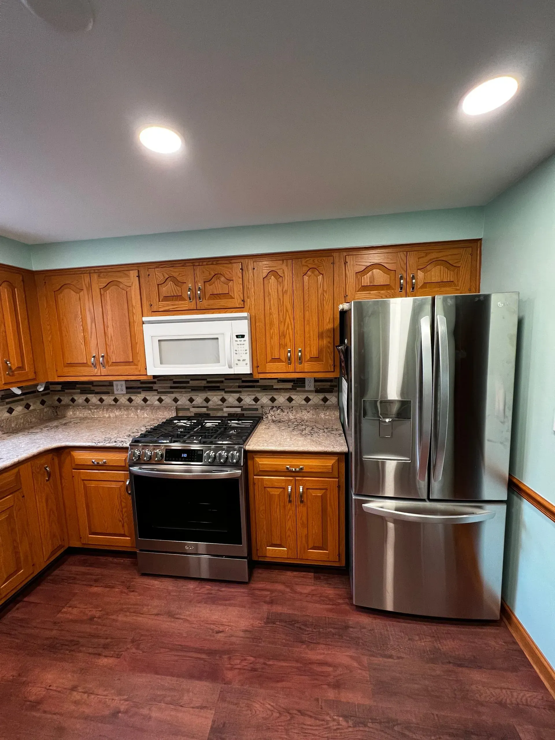 Kitchen with wooden cabinets, stainless steel appliances, and reddish-brown flooring. Light blue walls.