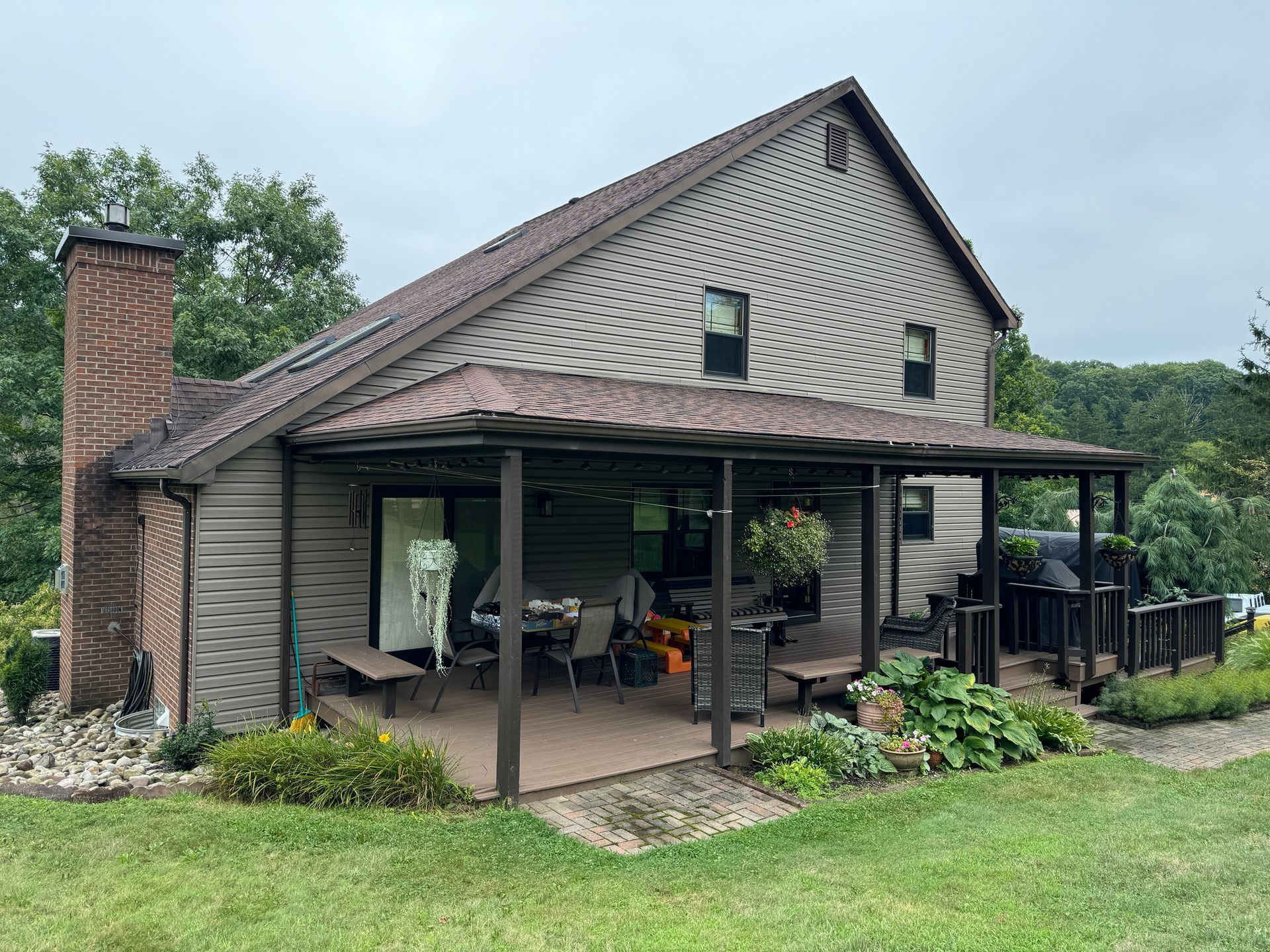 House with covered deck, brown siding, chimney, and lawn in a cloudy setting.