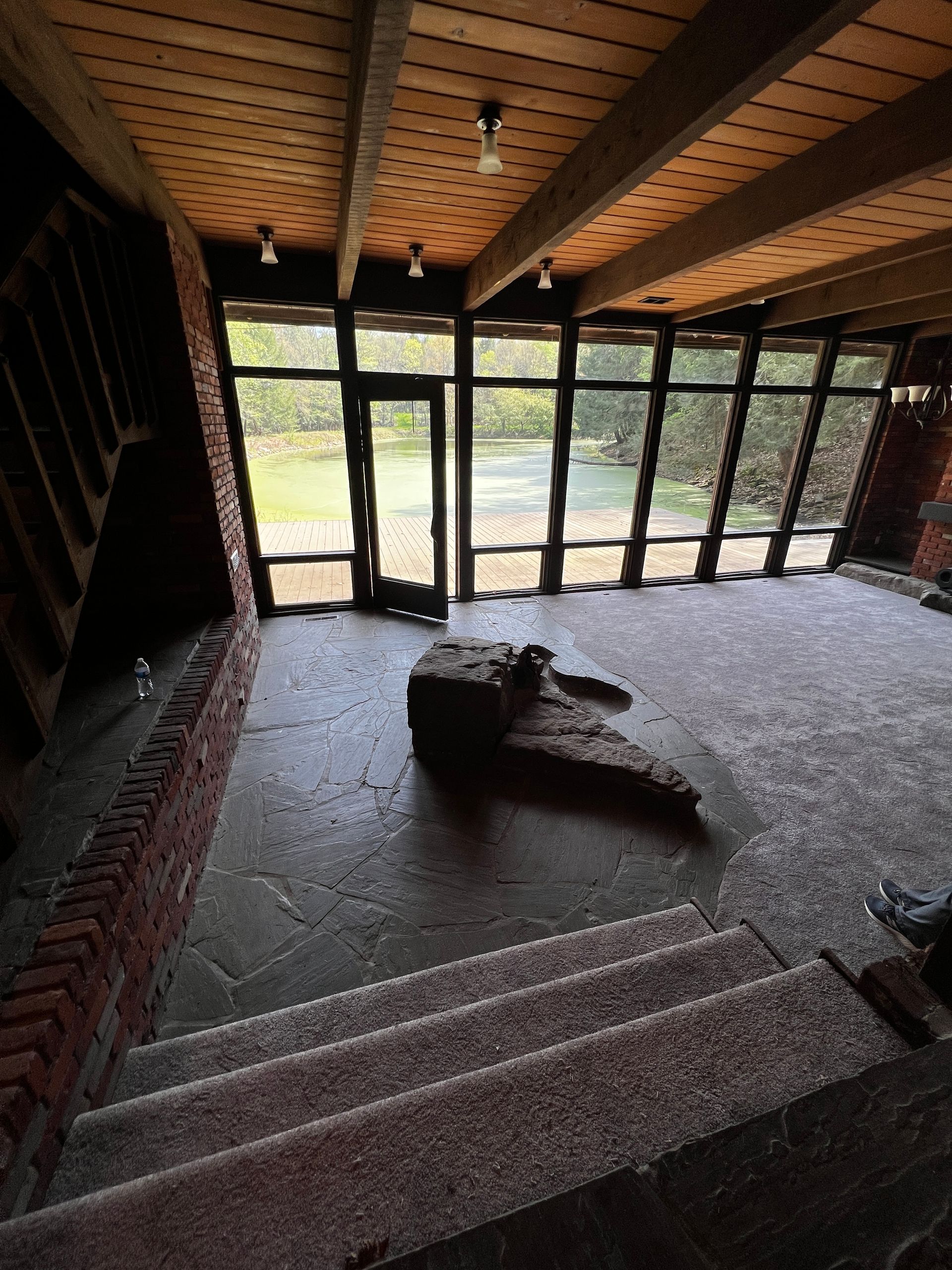 Interior view of a building with stone floor, brick accents, and glass windows. A stone sculpture sits in the center.
