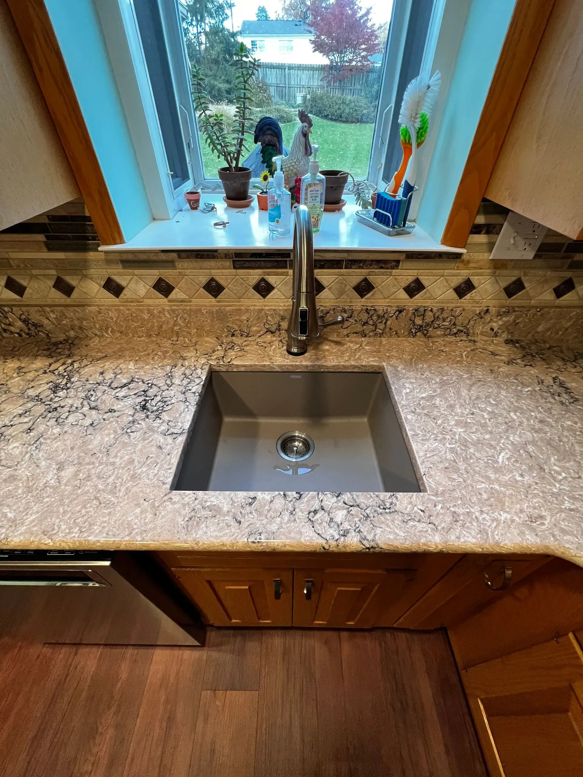 Kitchen sink with granite countertop and window view of a yard and trees.