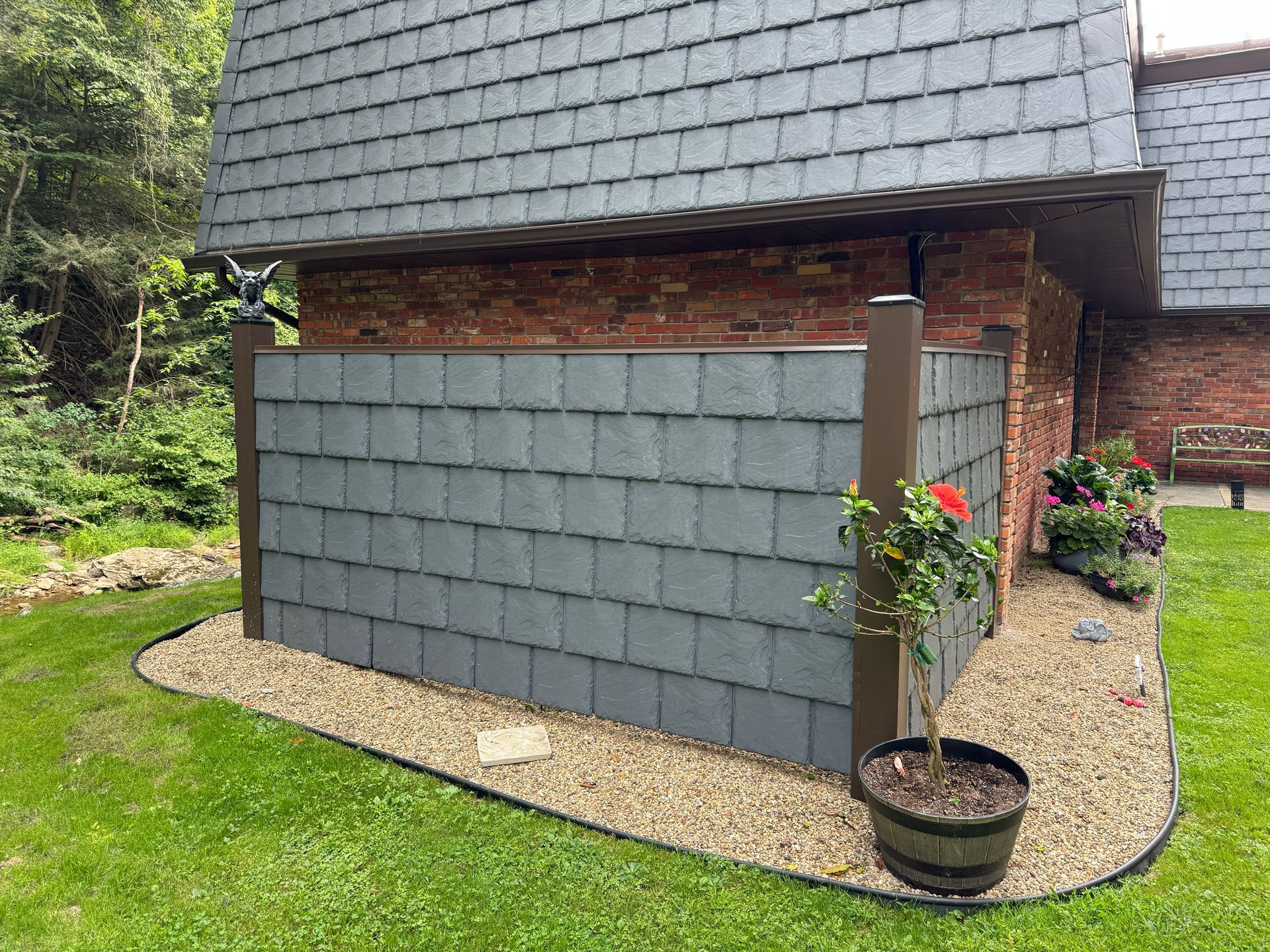 Gray shingled facade of a building with brick accents and gravel landscaping.