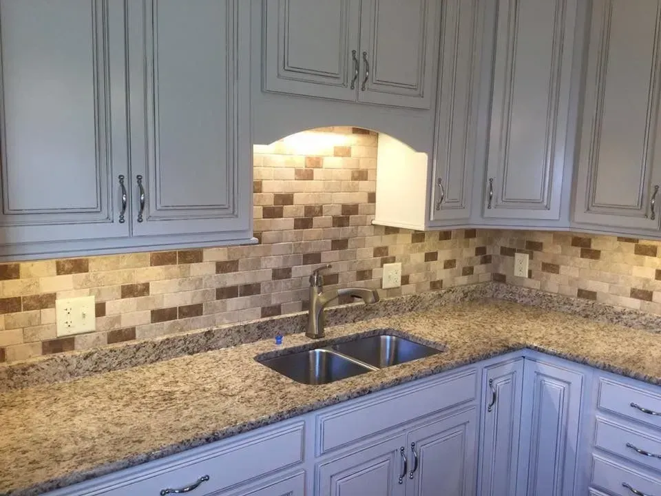 Kitchen with light-colored cabinets, granite countertop, mosaic tile backsplash, and stainless steel sink.