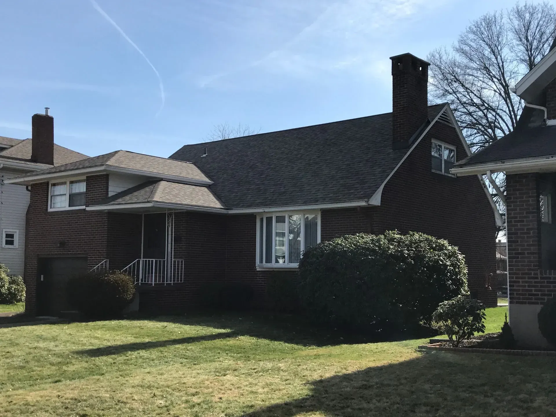 Brick house with dark roof and chimney, small yard, partly cloudy sky.