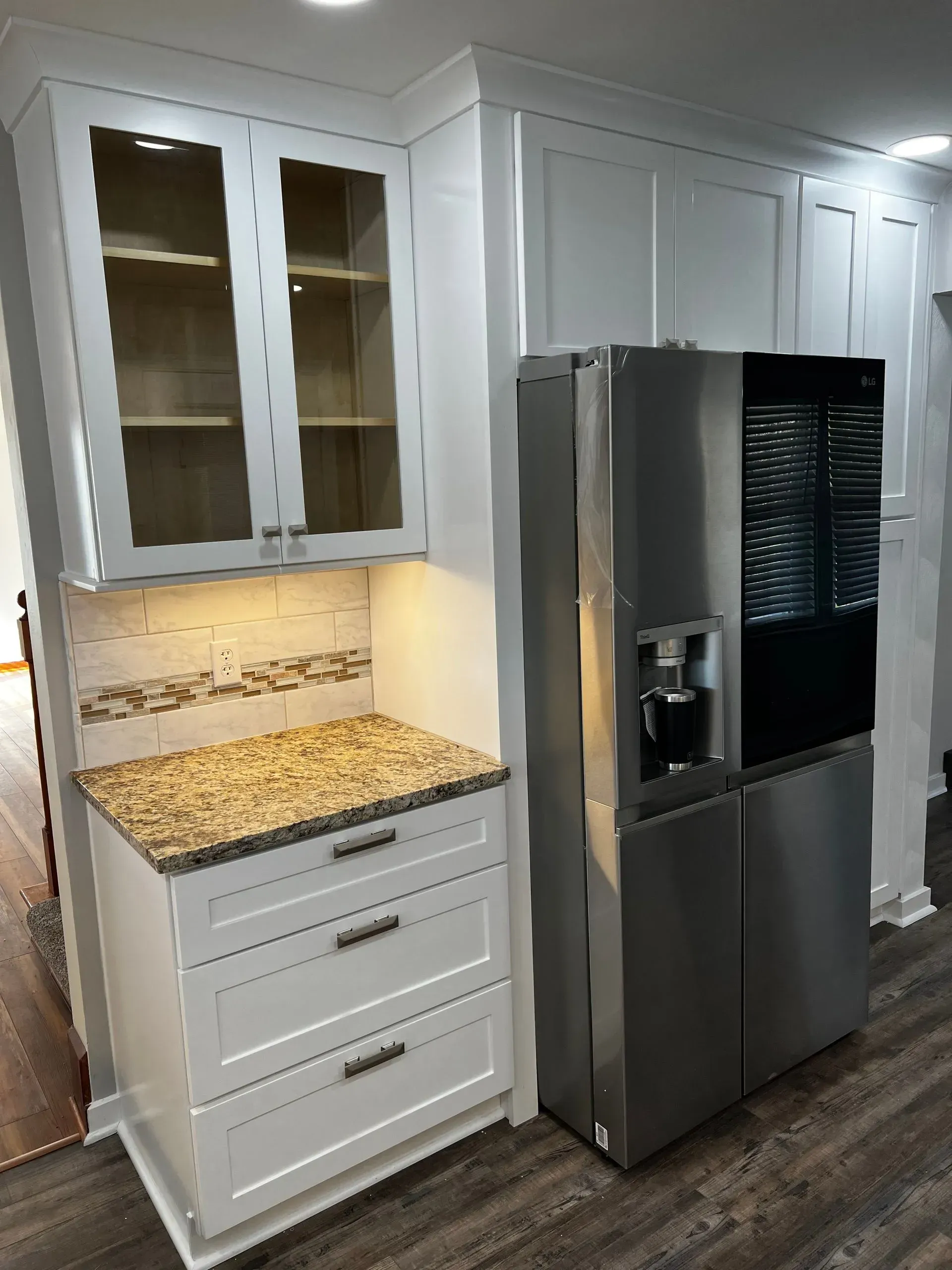 White kitchen cabinets with a stainless steel refrigerator next to a cabinet with granite countertop and drawers.
