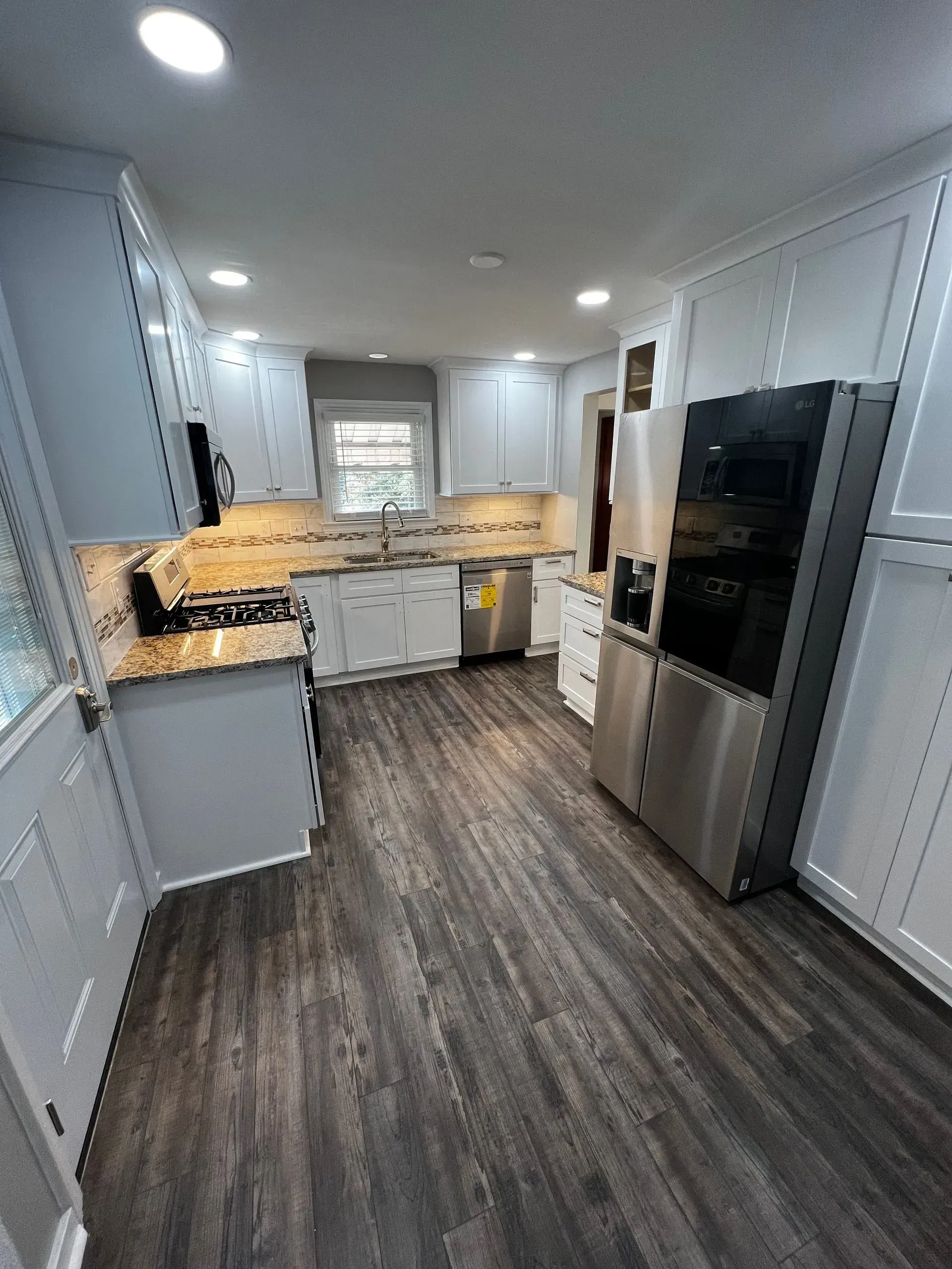 Kitchen with white cabinets, stainless steel appliances, and dark wood-look flooring.