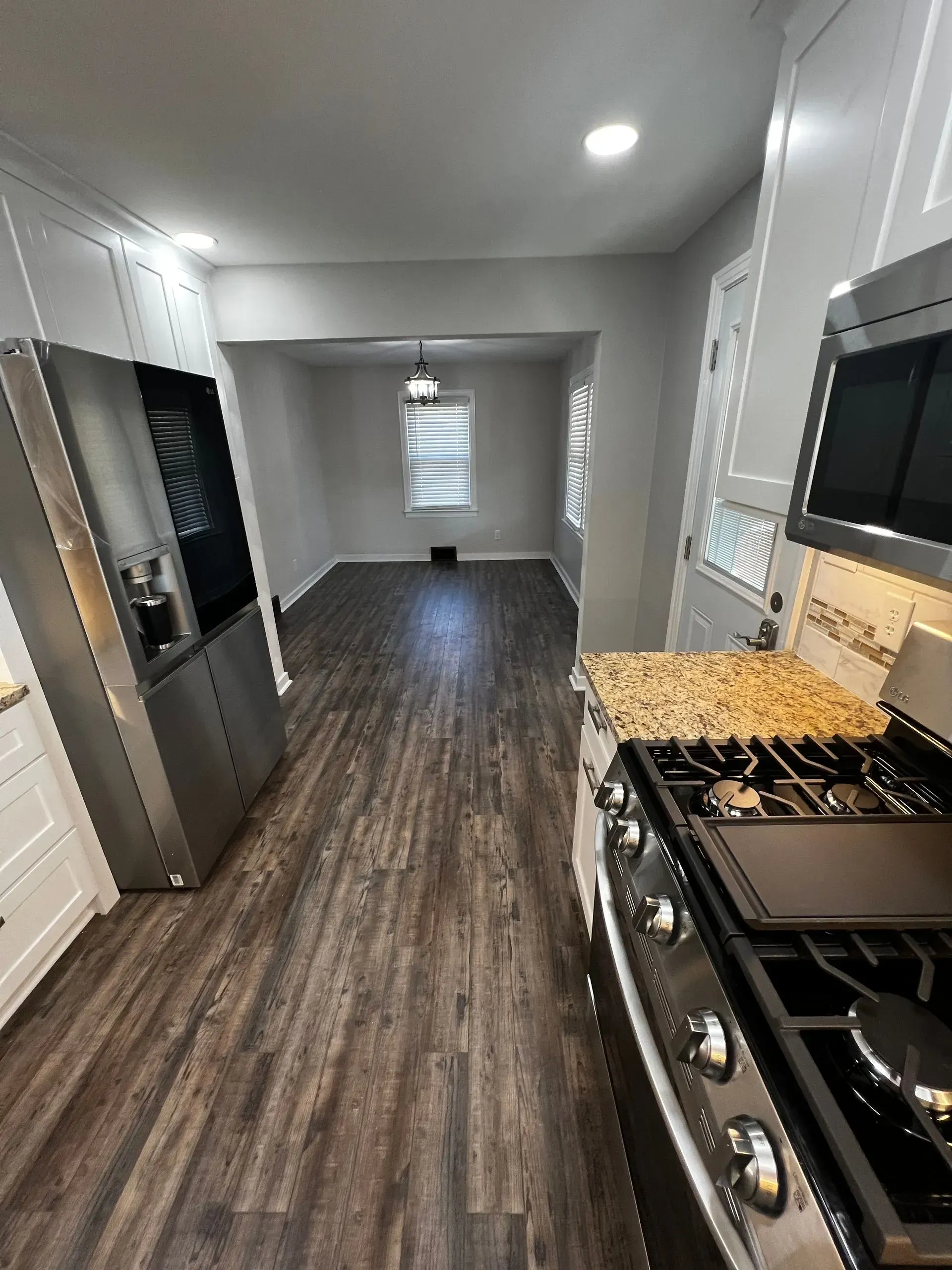 Kitchen interior with stainless steel appliances, dark wood flooring, and view into the dining area.