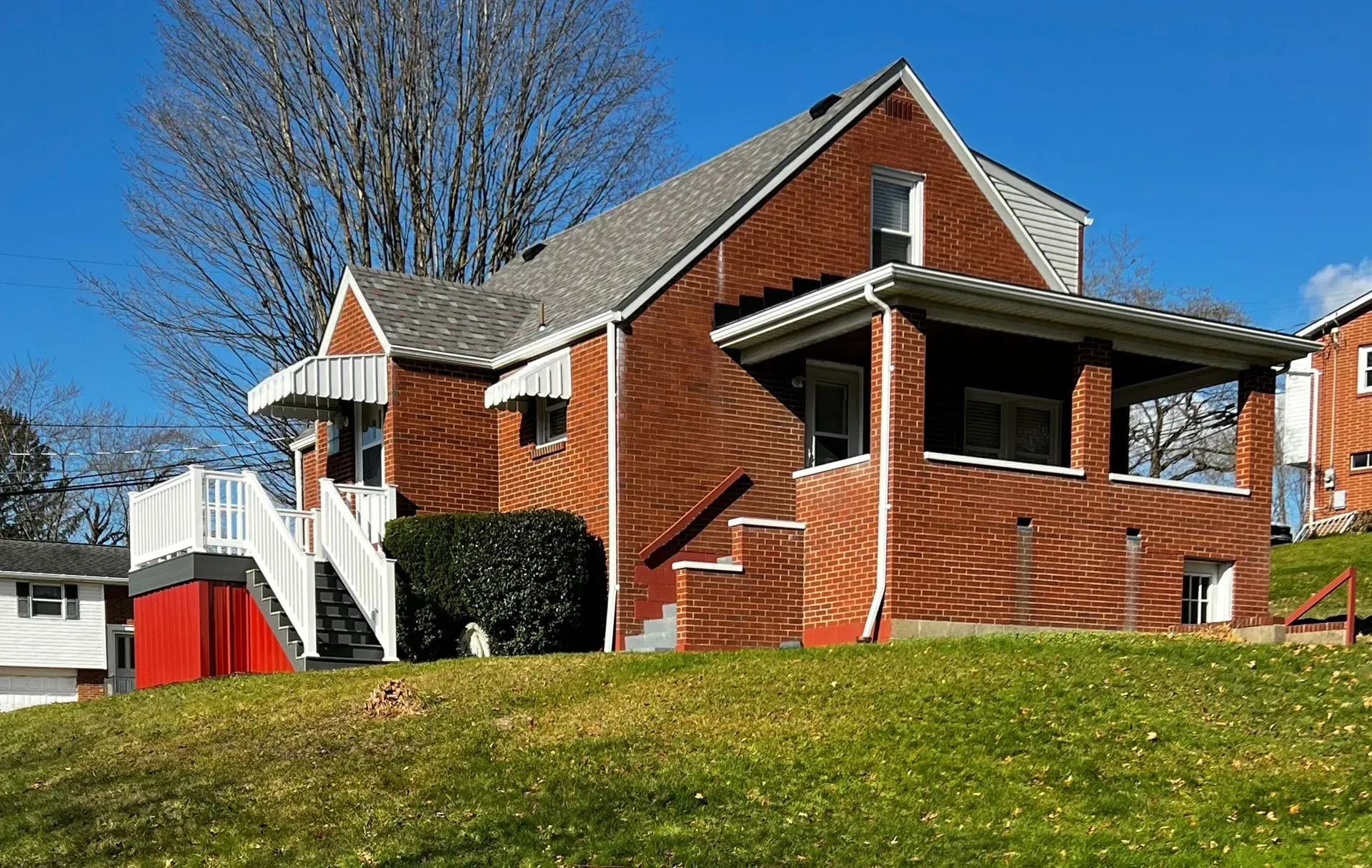 Brick house with covered porch, white stairs, and green lawn under a blue sky.
