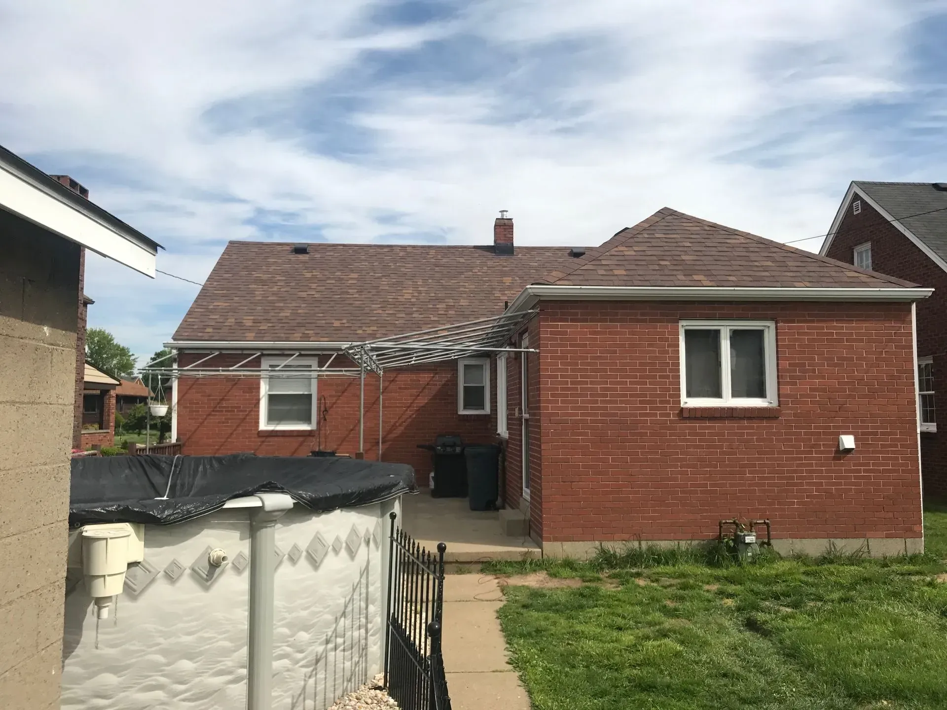Backyard view of a brick house with a brown roof, a small above-ground pool, and a partial view of a neighboring house.