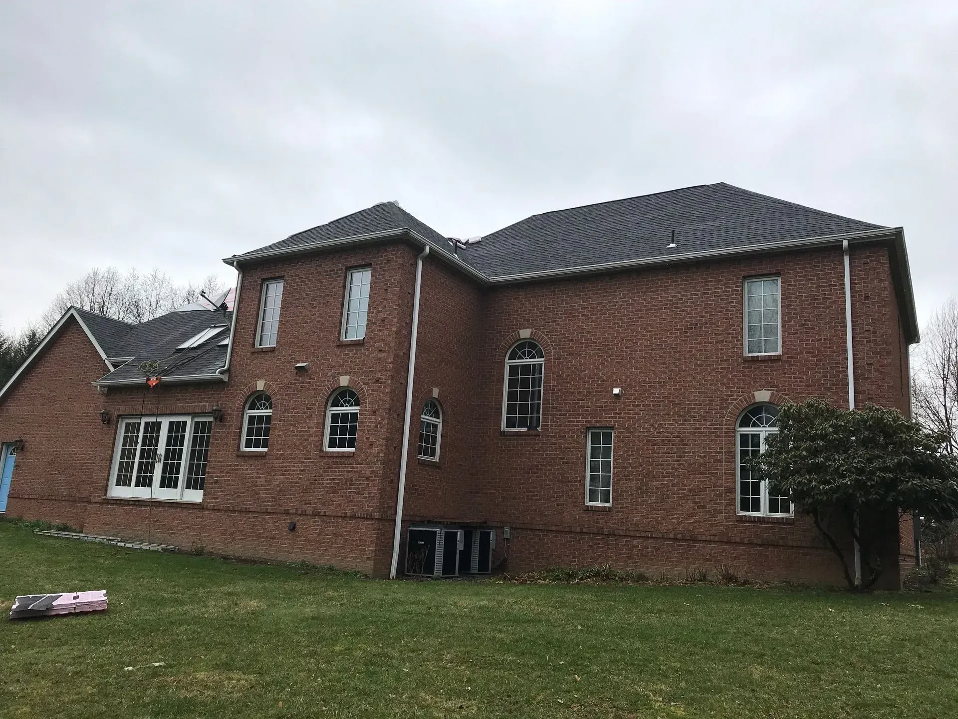 Red brick house with multiple windows, gray roof, and overcast sky.