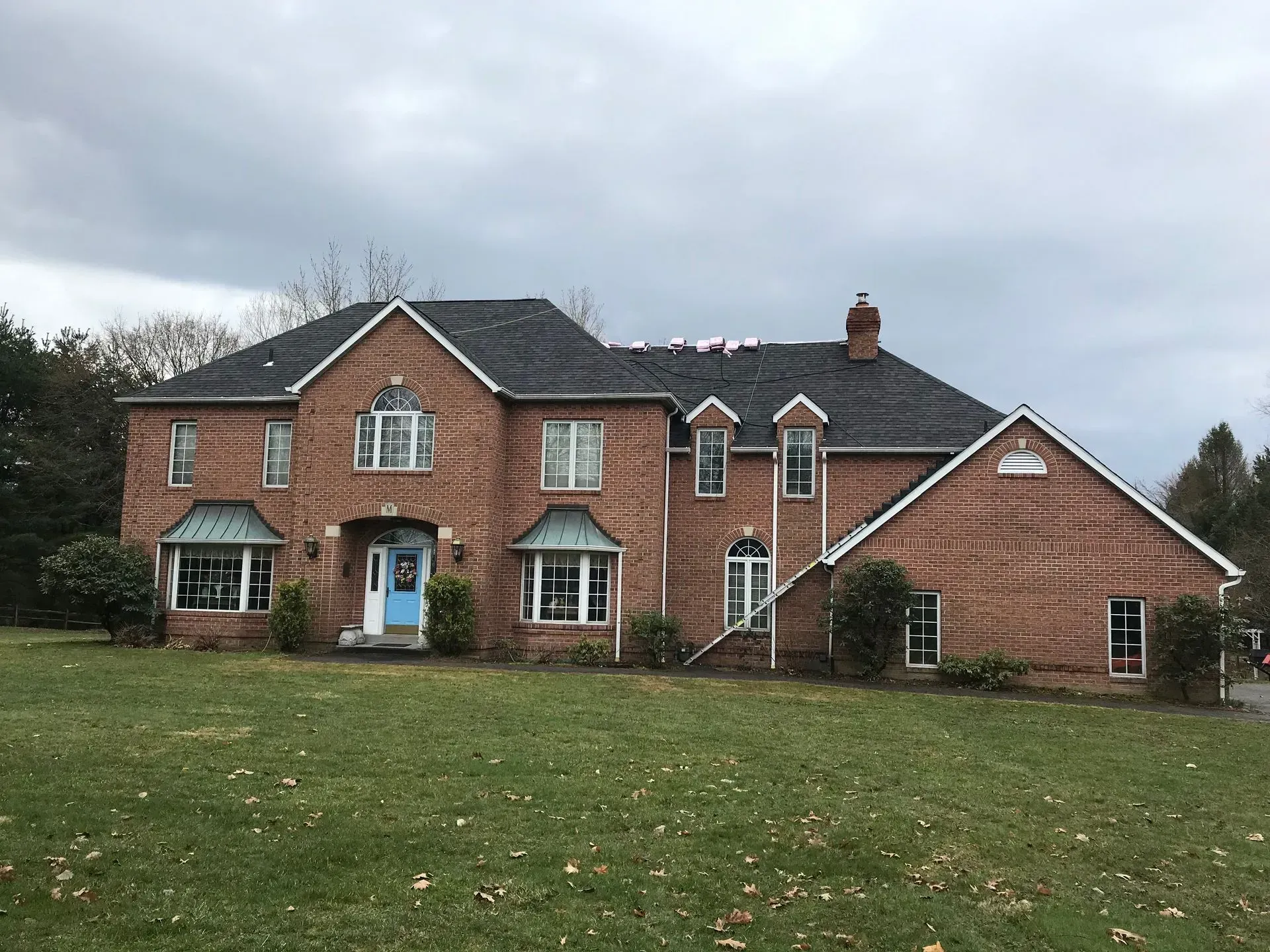 Red brick two-story house with blue door and dark roof under cloudy sky; grass lawn in front.