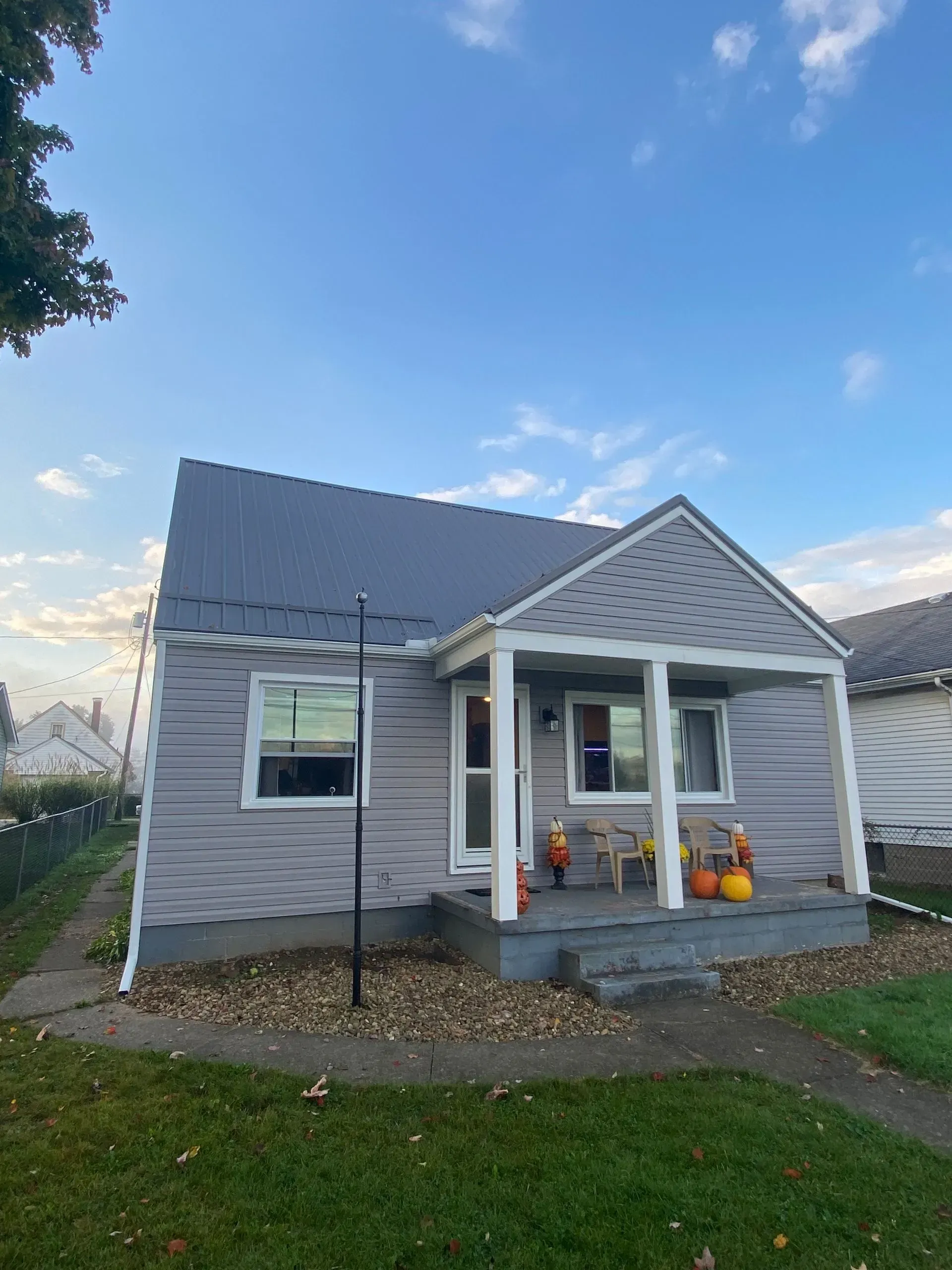 Gray bungalow with porch, pumpkins, and a blue sky.