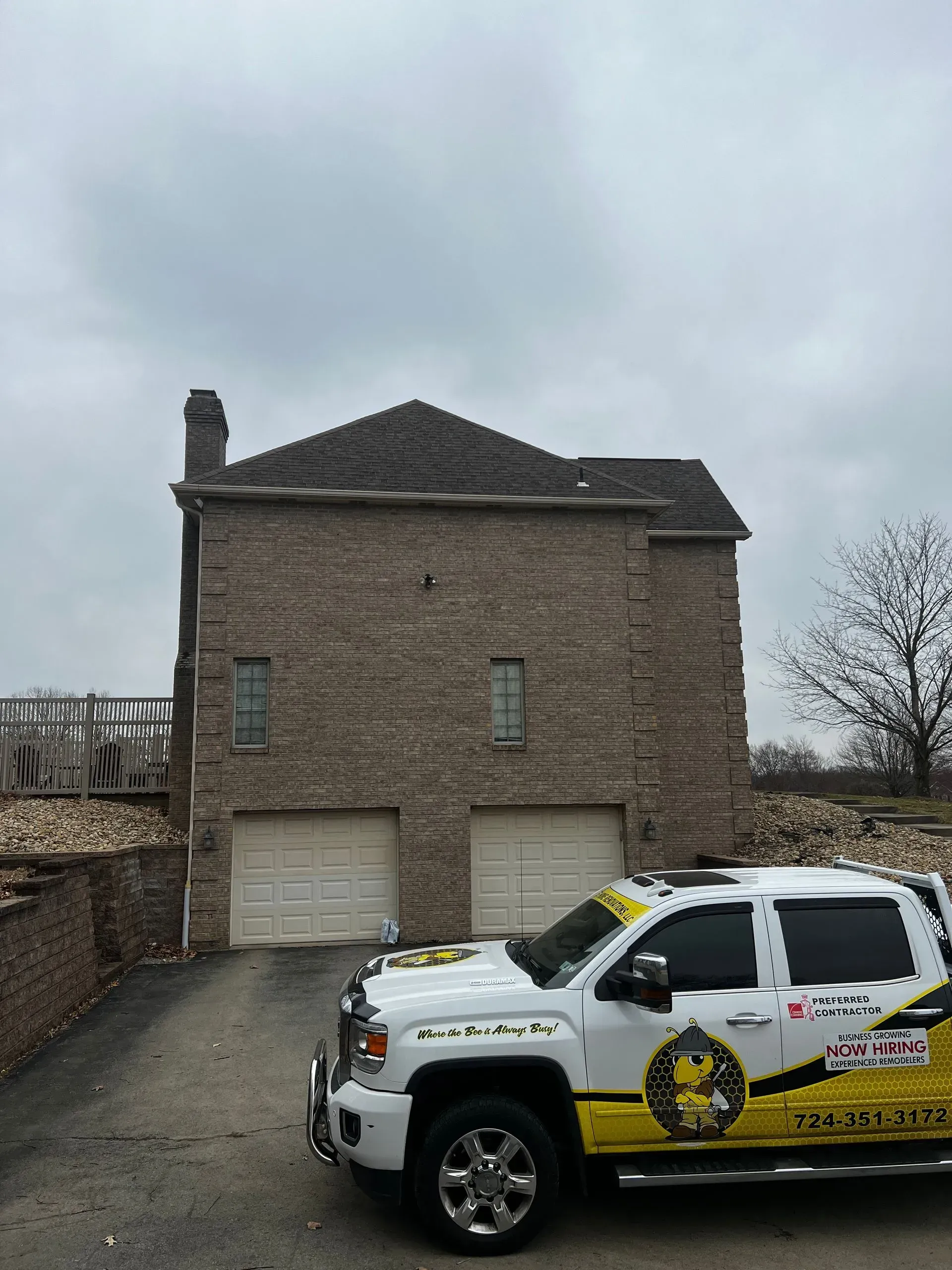 White truck parked in front of a brick building with a brown roof and two garage doors on a cloudy day.