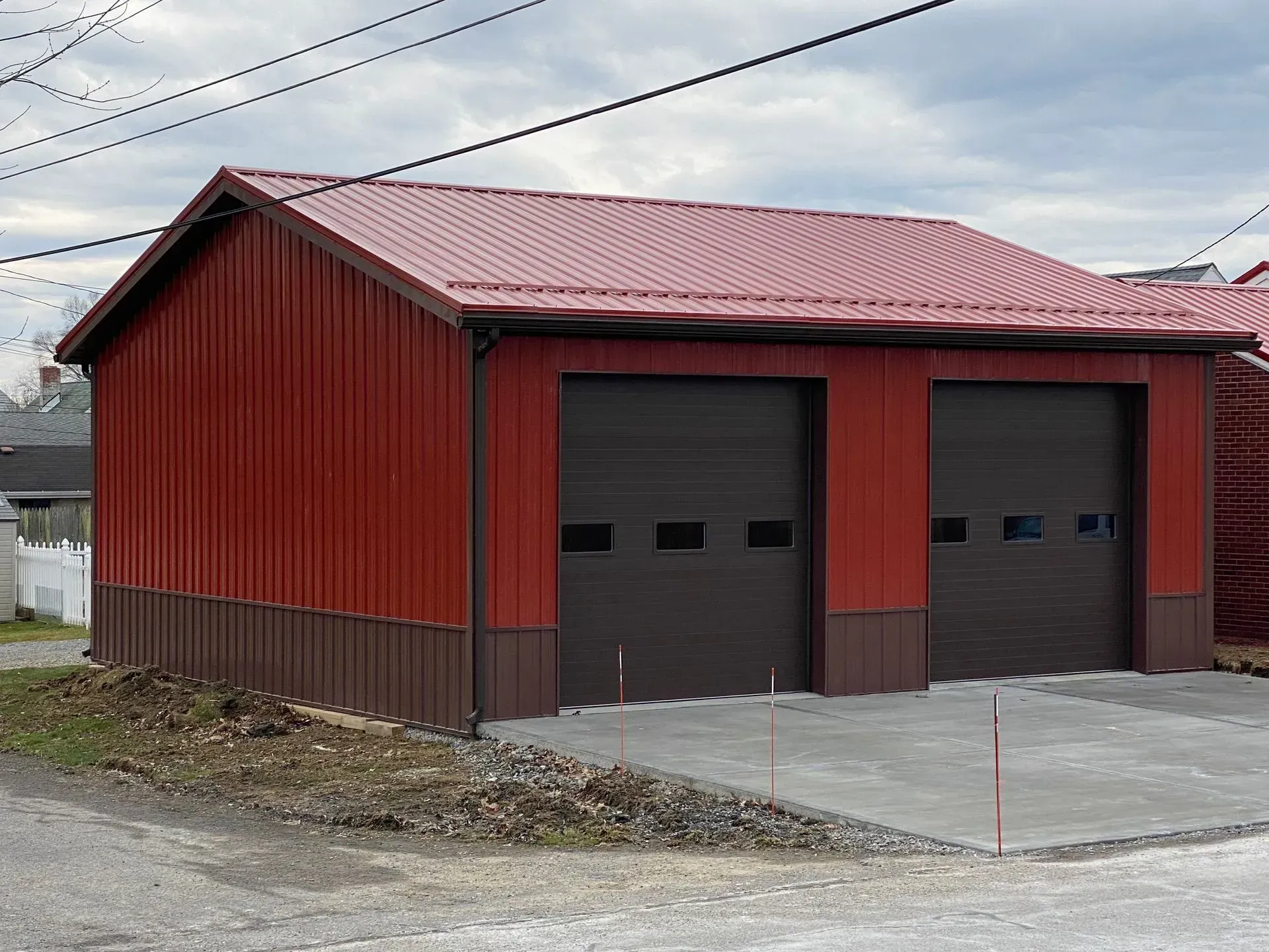 Red and brown metal garage with two doors and a concrete driveway.