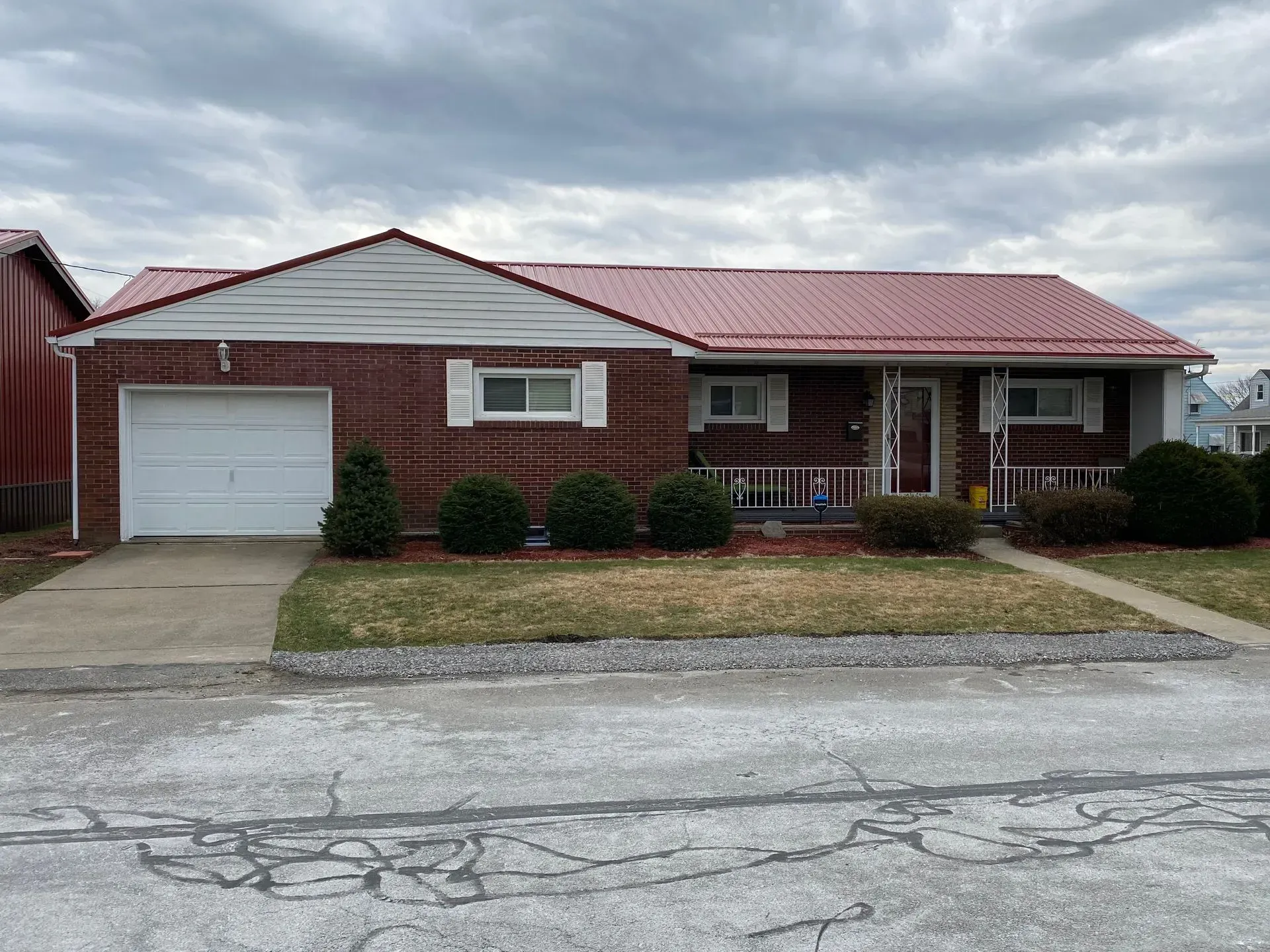 Brick ranch home with red metal roof, white garage door, and small front porch.