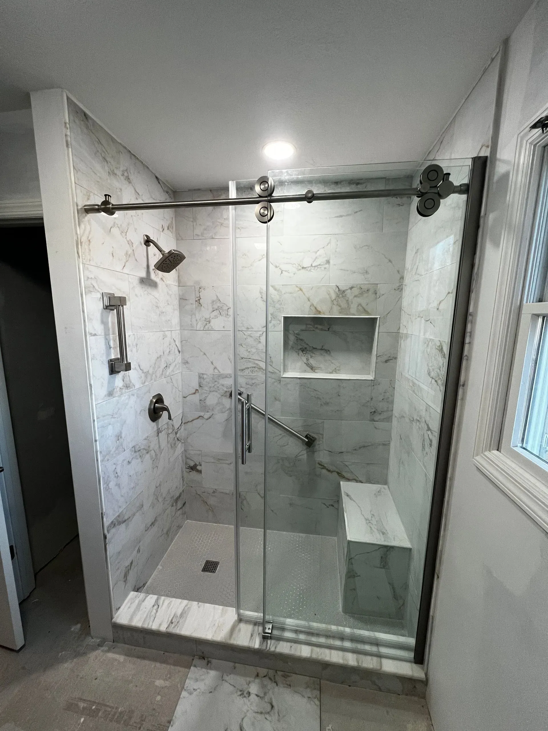 Newly renovated shower with marble tile, glass door, and built-in bench.