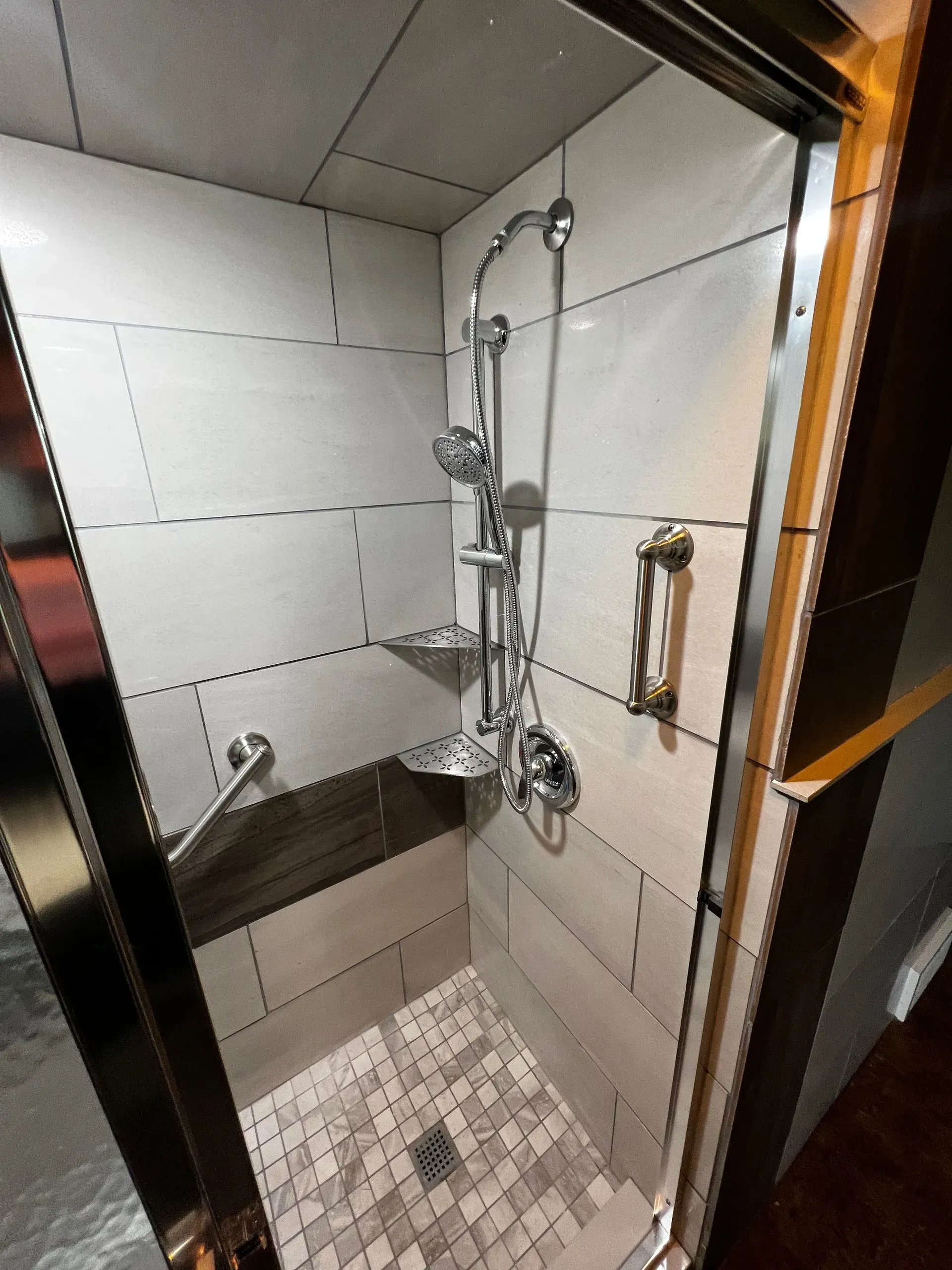 A shower with white and wood-tone tiles, chrome fixtures, and glass doors.