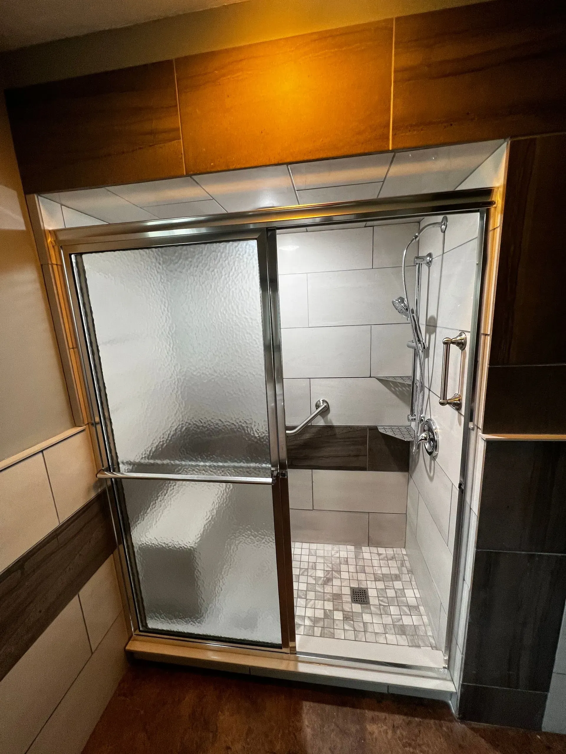 Shower with frosted glass doors, tiled walls, and patterned floor.