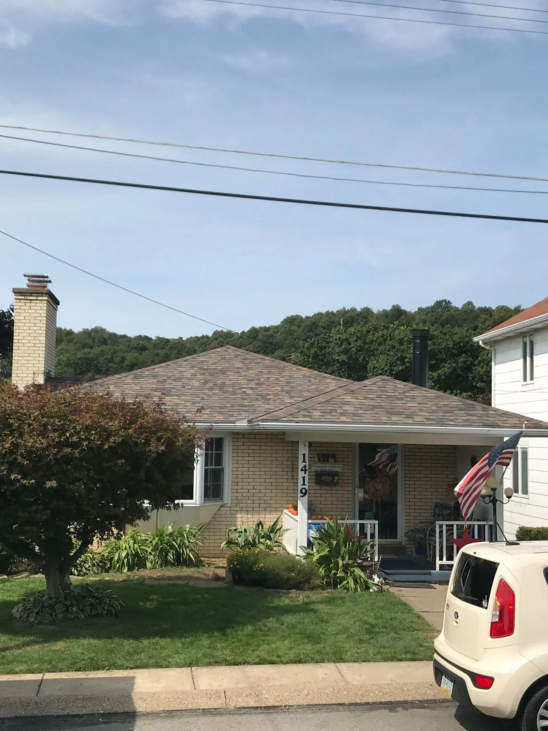 Small, yellow brick house with a brown roof and a small yard with a white car parked in front.