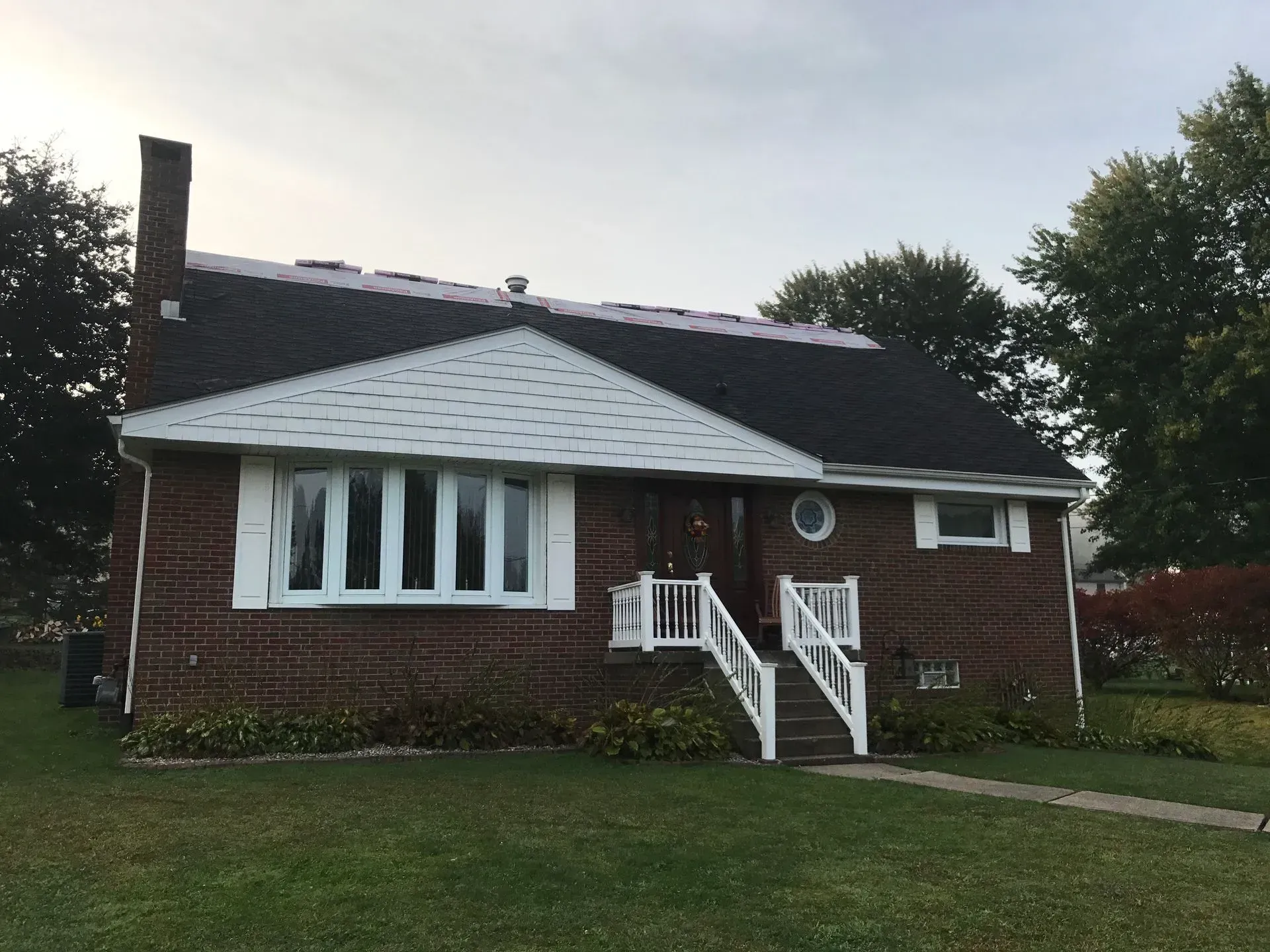 Brick house with white trim, dark roof, and a chimney on a cloudy day.