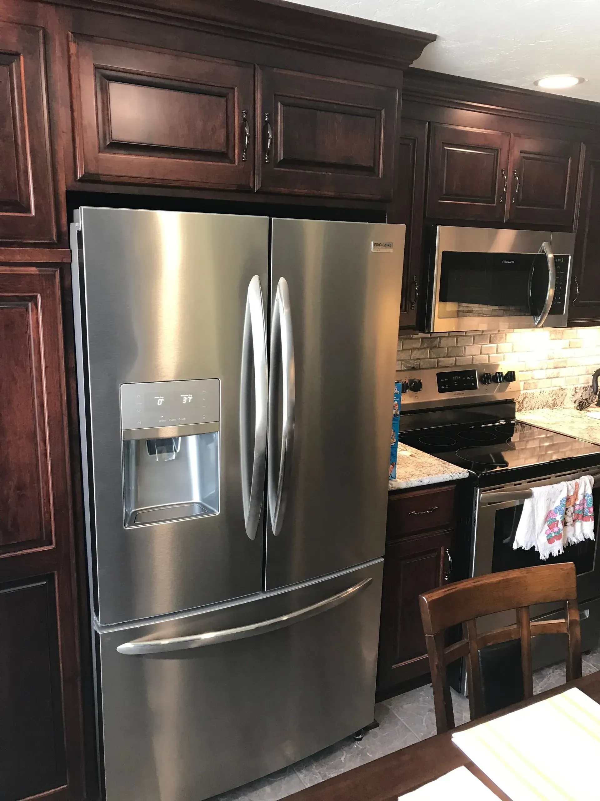 Stainless steel refrigerator in a kitchen with dark wood cabinets and a microwave.