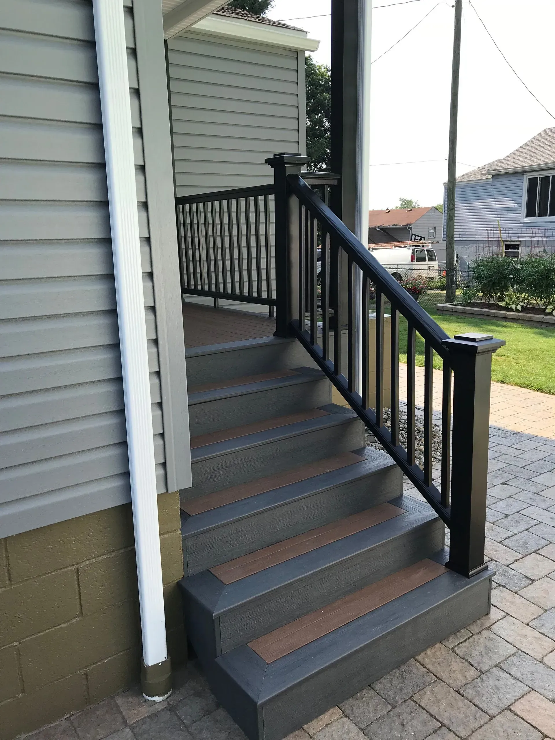 Exterior steps with black railing, leading to a porch with gray siding.
