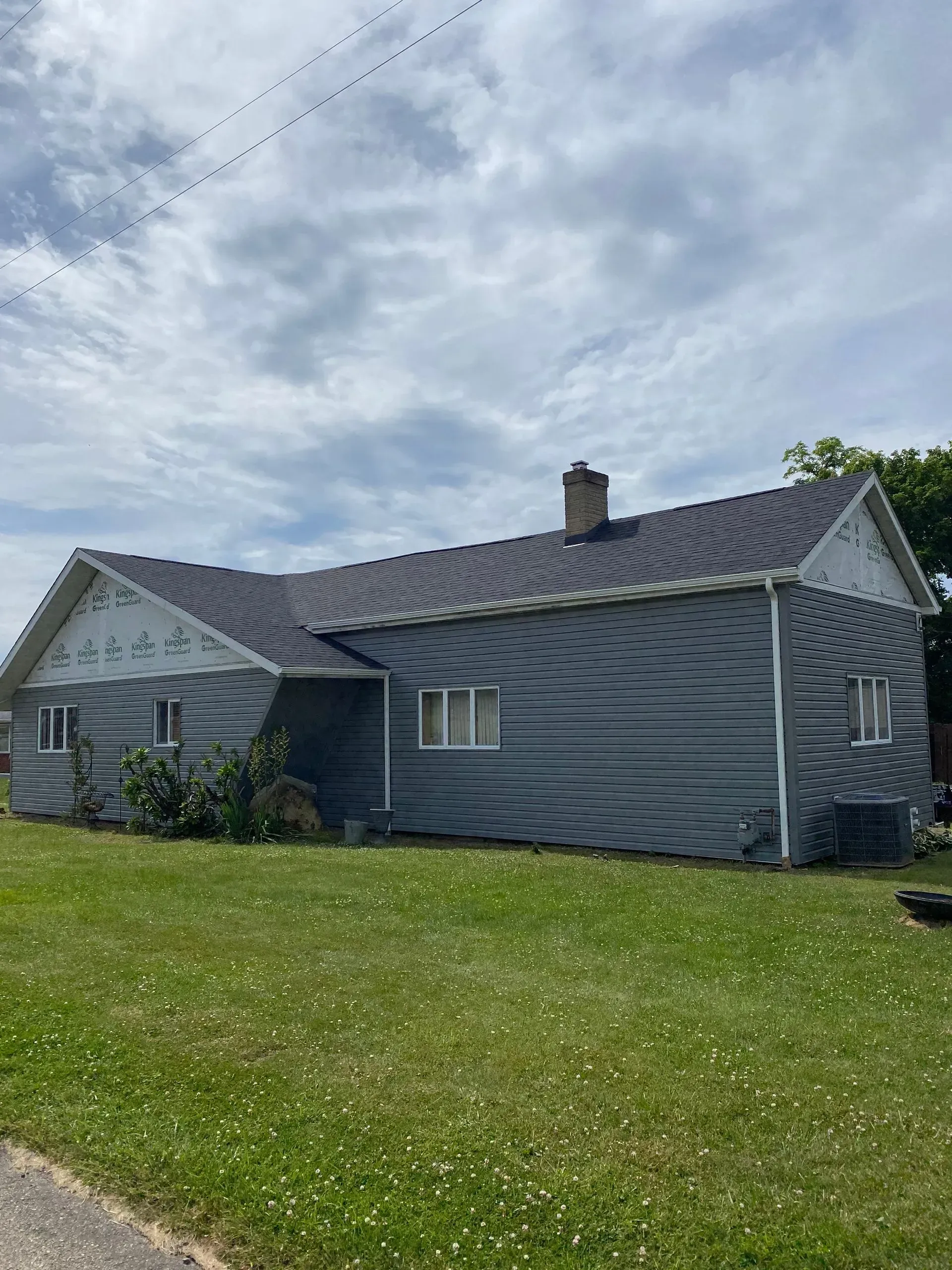 Gray house with dark roof and green lawn under a cloudy sky.
