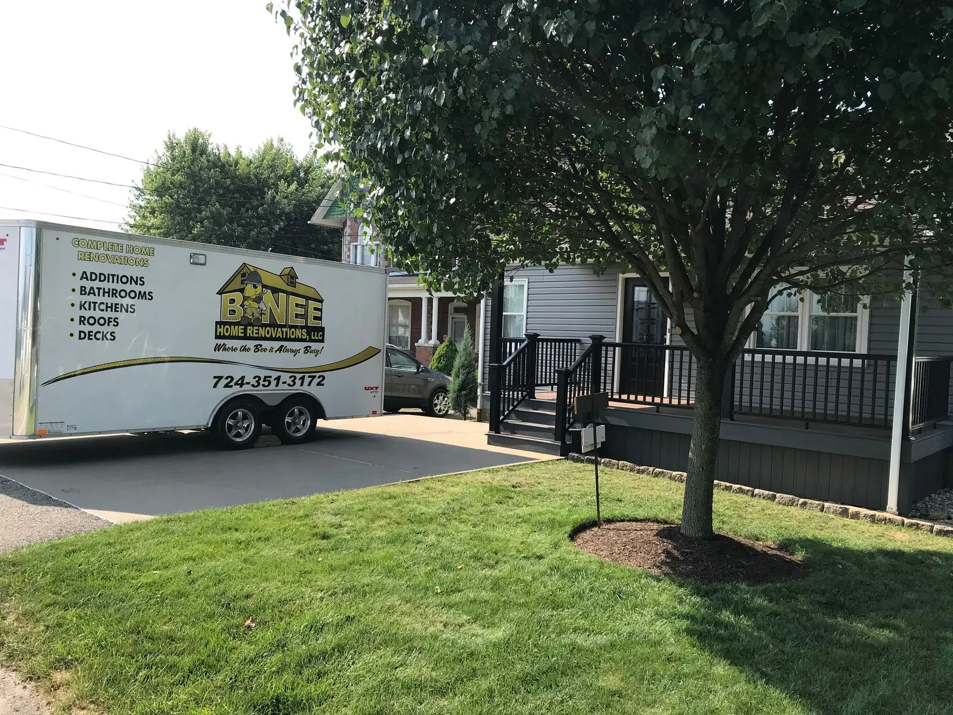 A white trailer parked in front of a gray house. A tree is in the foreground.