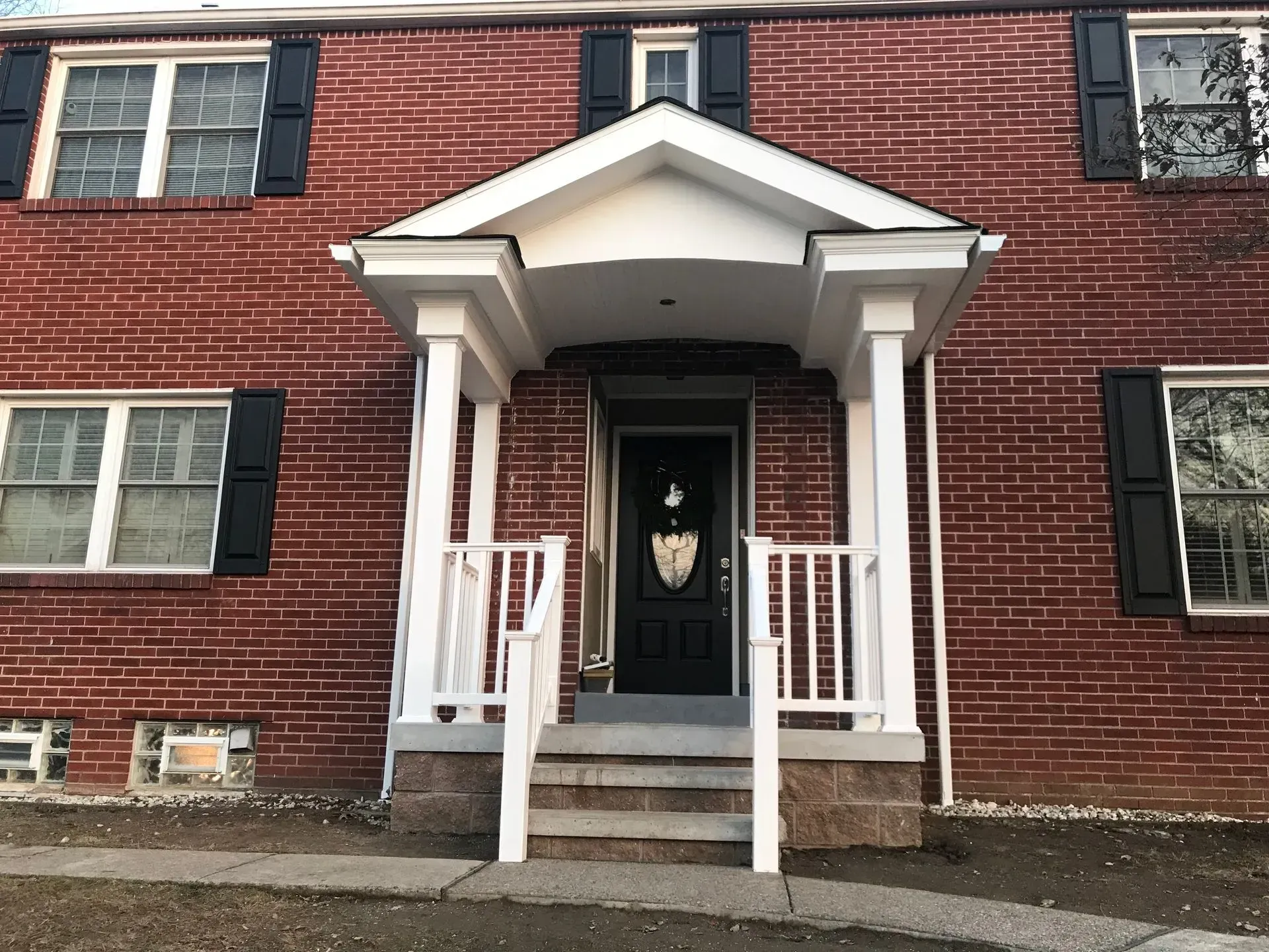 Red brick building with white porch, pillars, and black shutters on windows.
