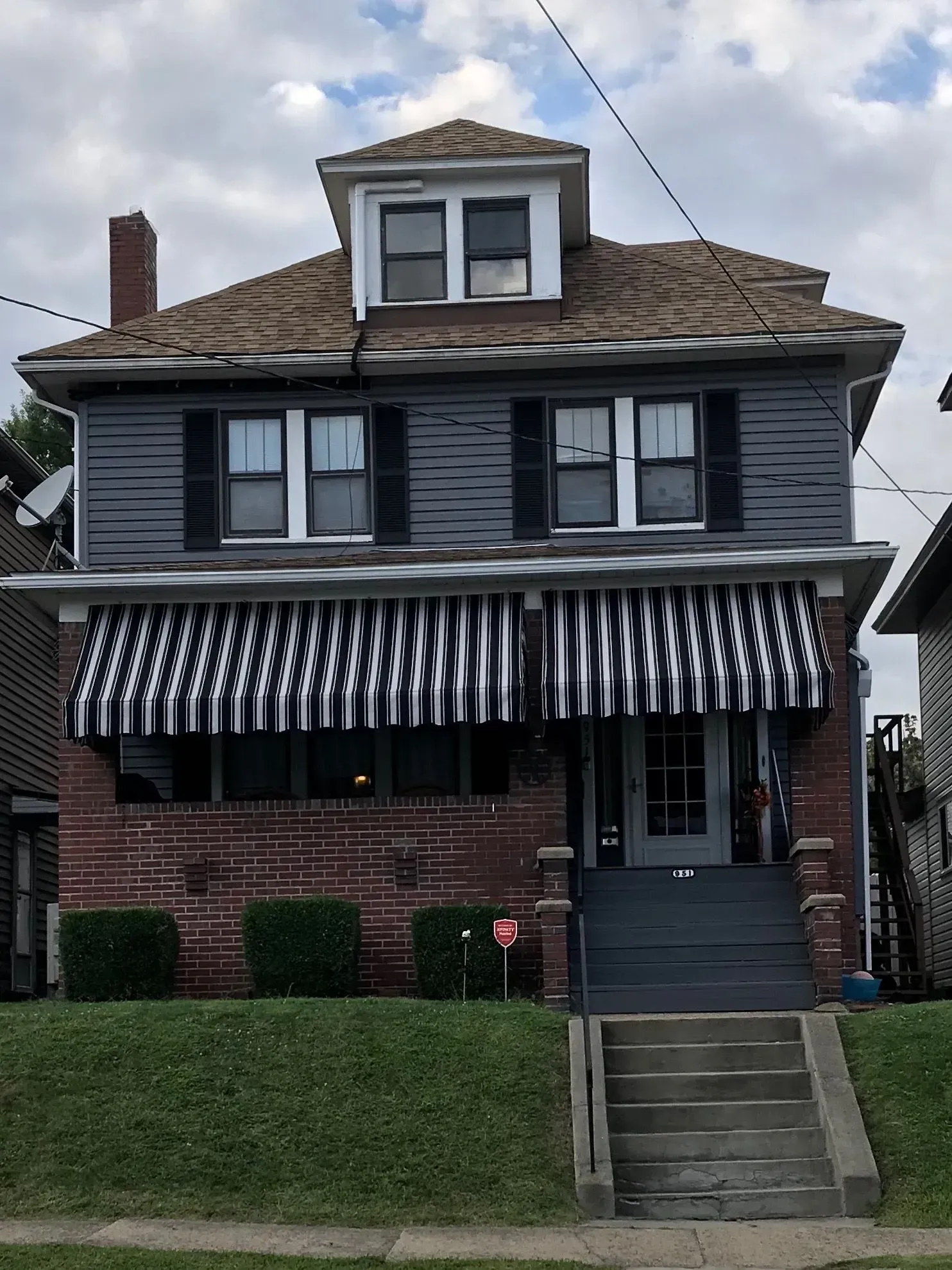 Two-story house with brick base, awnings, and steps leading to the front door.