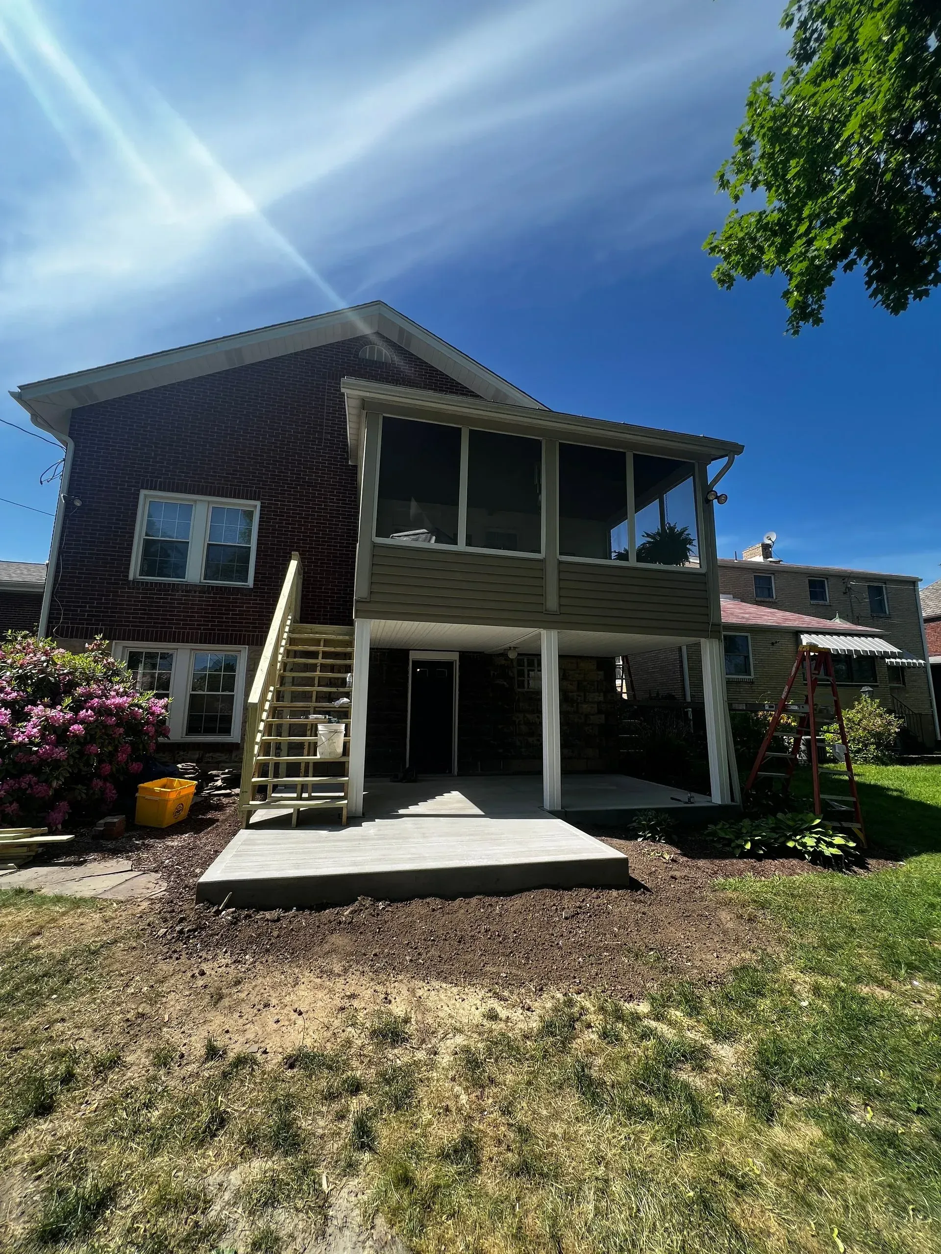Backyard with a two-story home, deck, and concrete patio. Blue sky with white clouds.