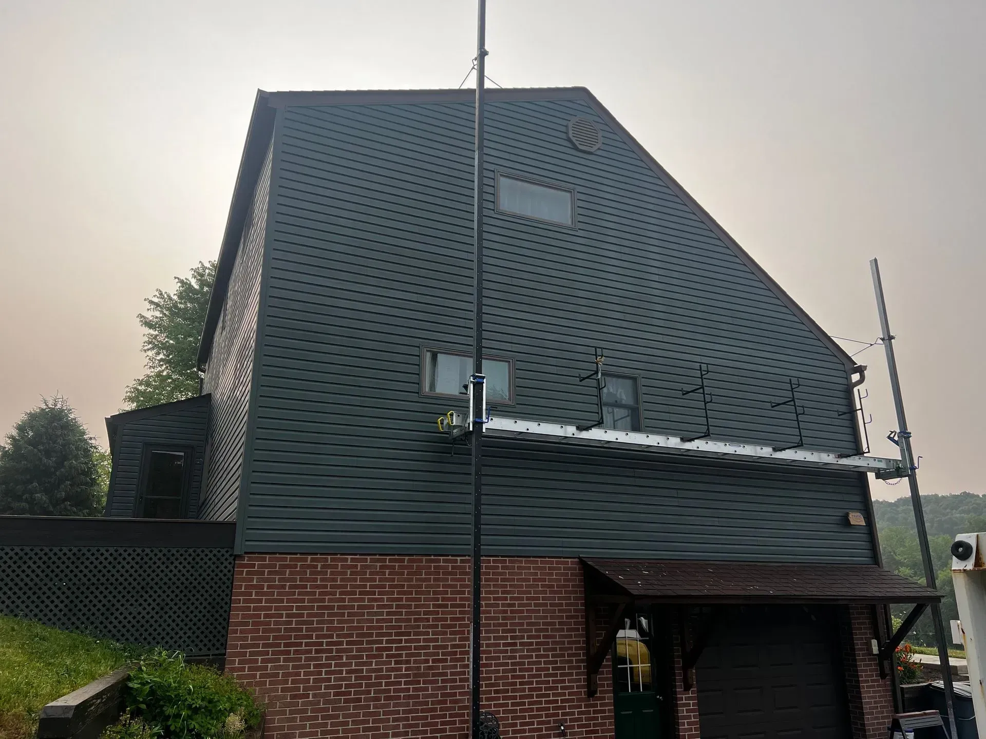 Dark-sided building with dark shingled roof and brick base. A pole with equipment is attached to the side.