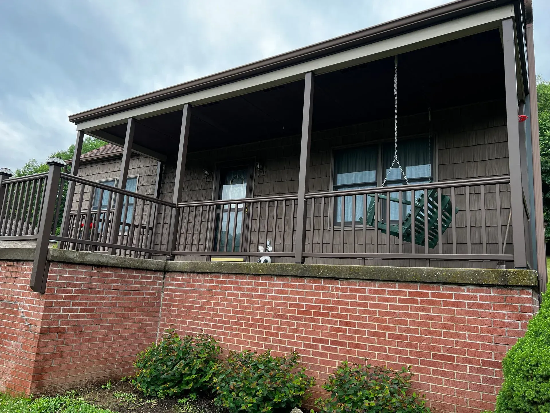 Brown cabin with brick base, covered porch, and small shrubs in front.