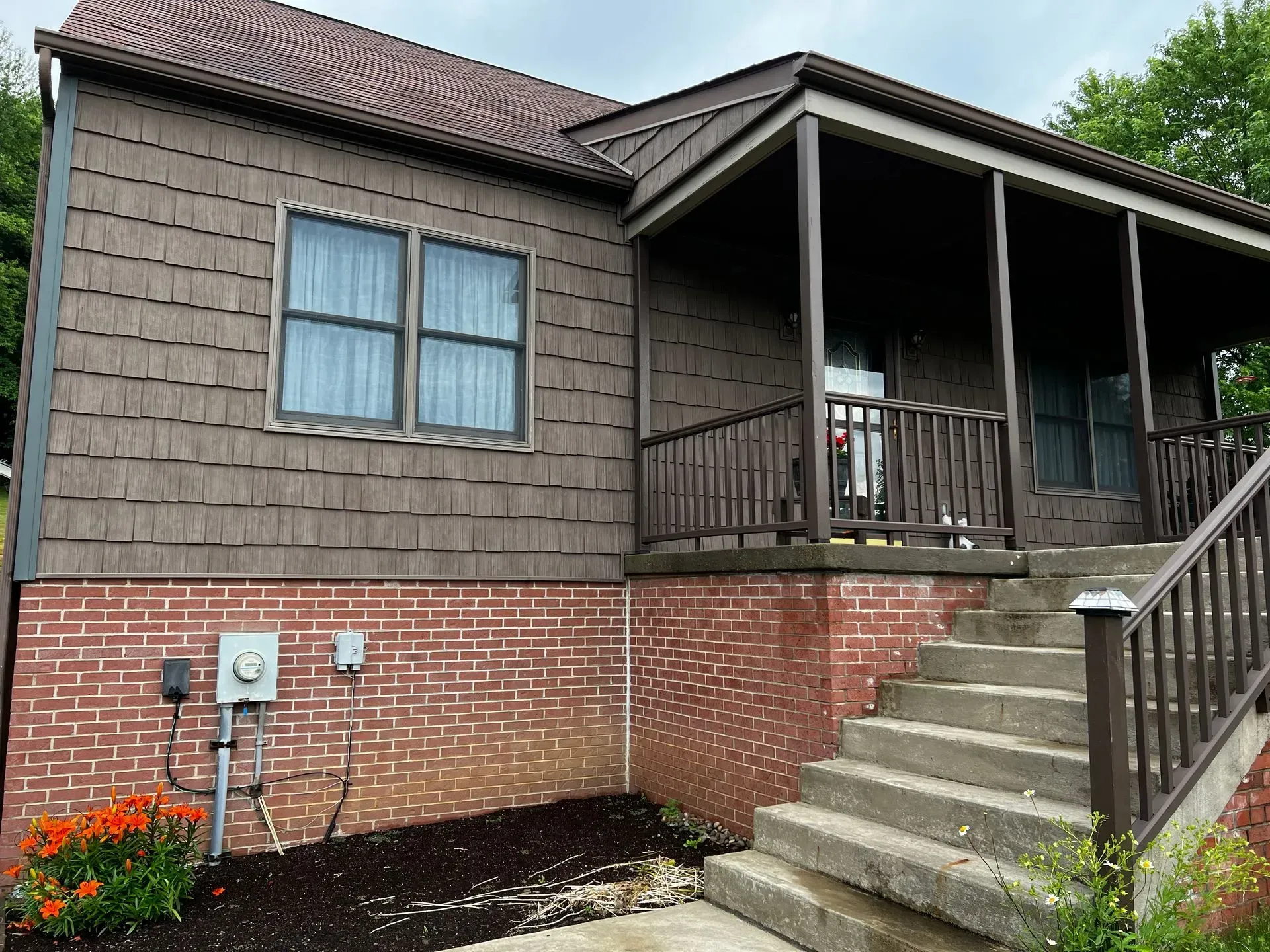 Brown house with porch, brick foundation, and concrete steps.