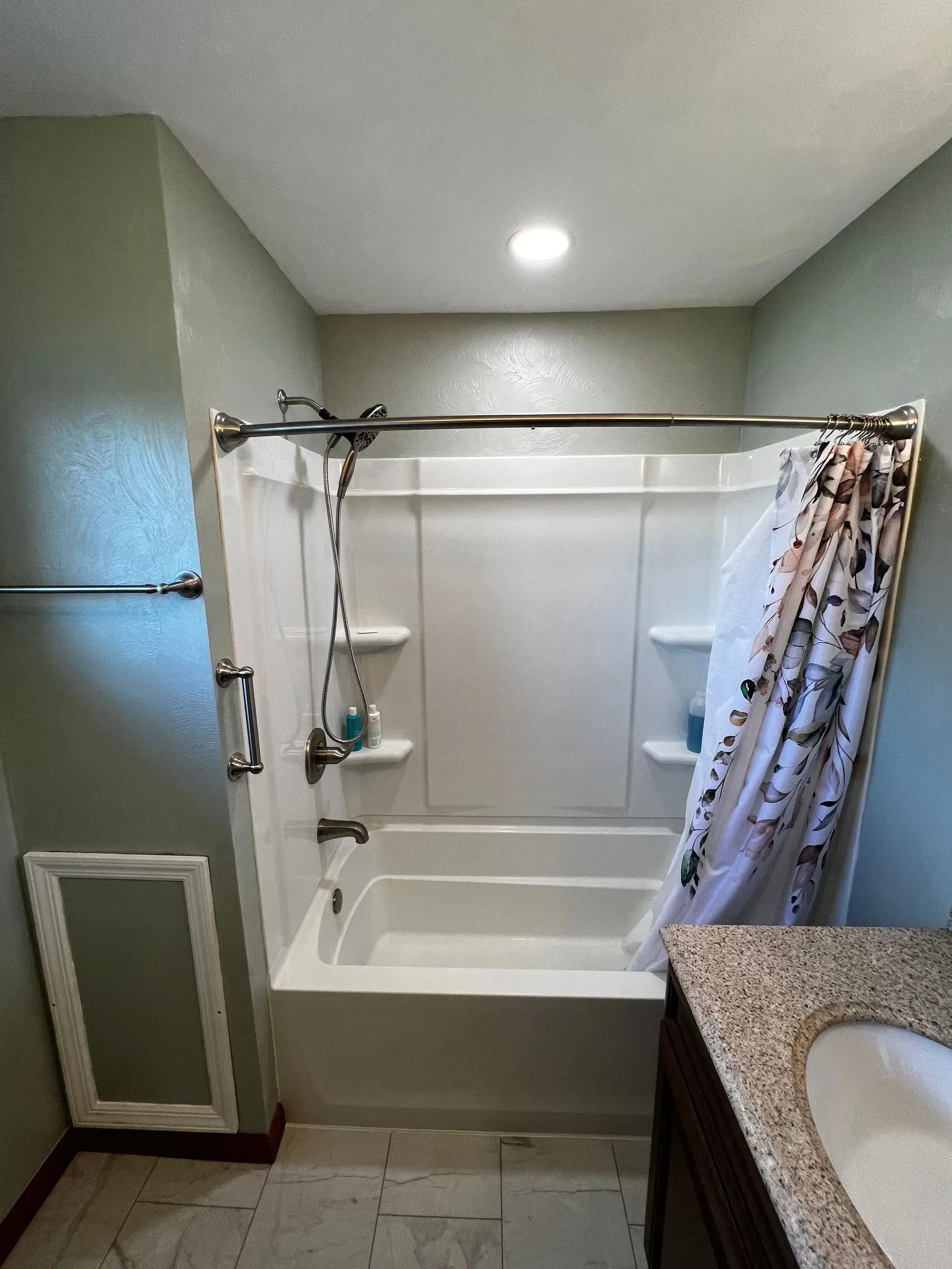 Bathroom with a white bathtub and shower surround, light green walls, and a patterned shower curtain.