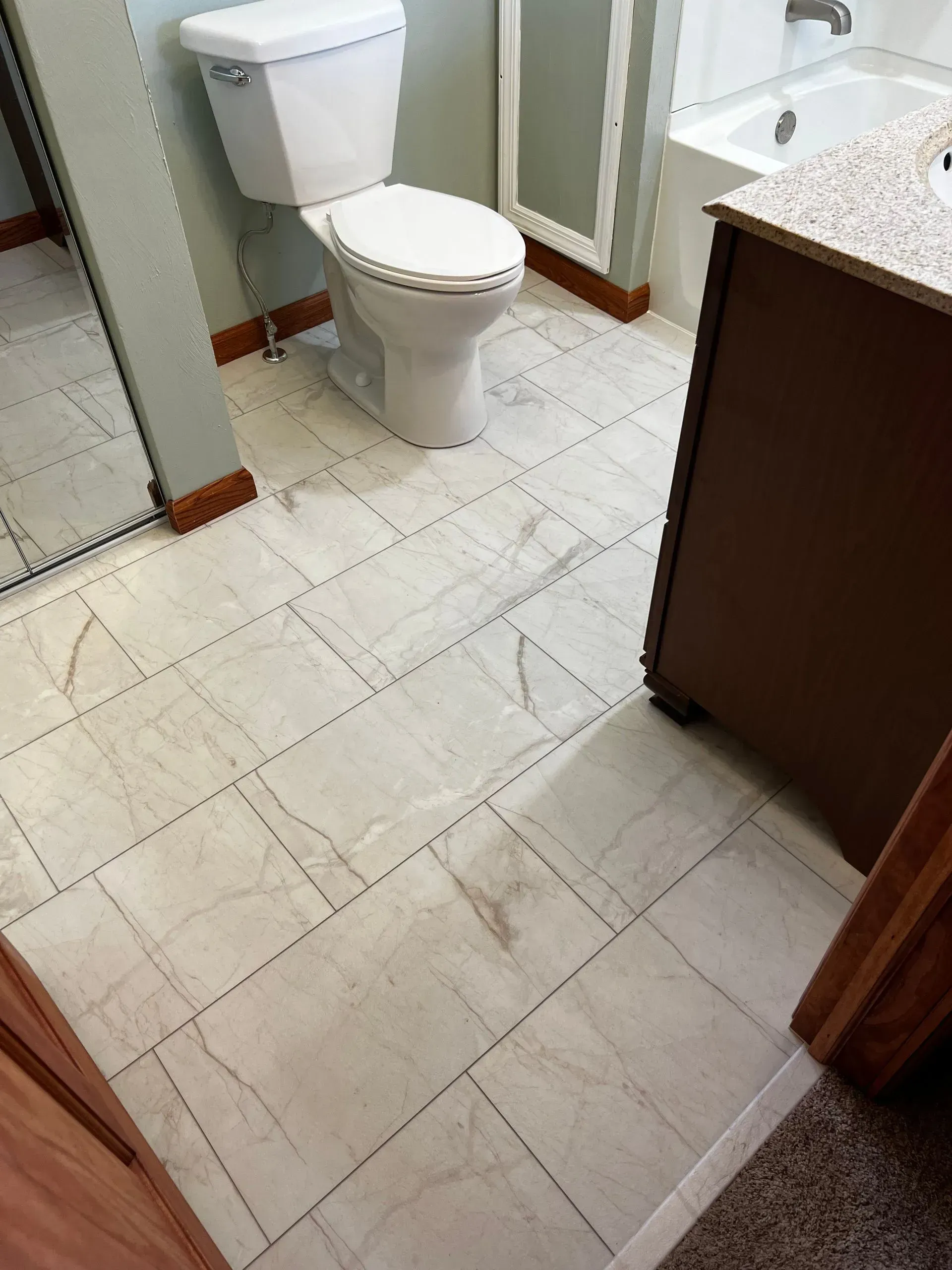 Bathroom with light-colored tile floor, toilet, vanity, and shower area.