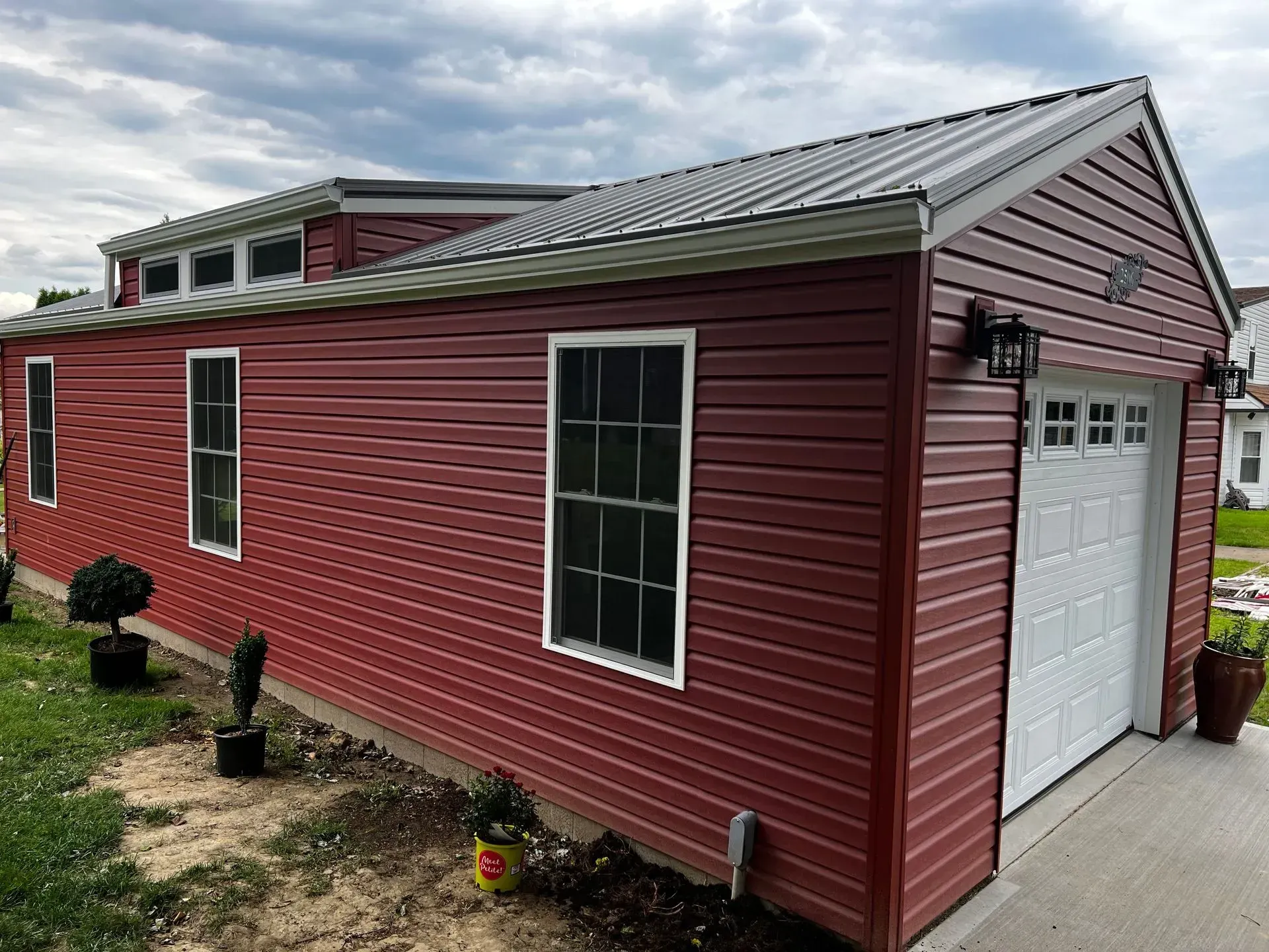 Red metal-sided building with white garage door and windows, gray metal roof, and landscaping.