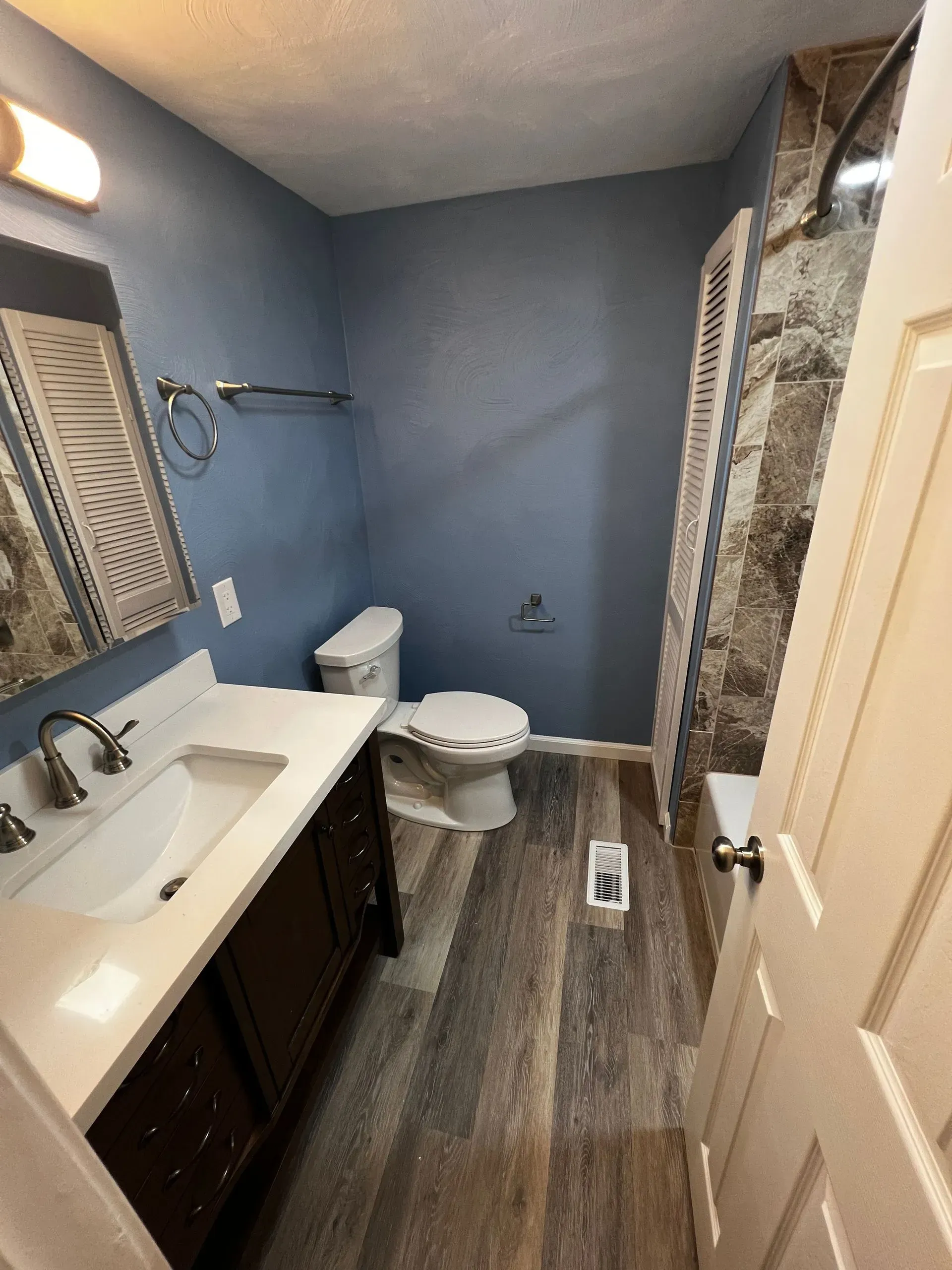 Bathroom with blue walls, dark vanity, and wood-look flooring. A toilet and shower are visible.
