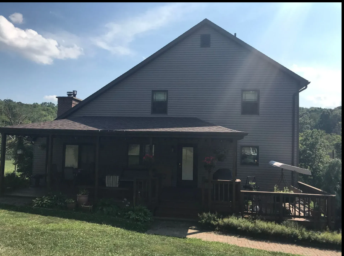 dark gray house with porch and deck, set in a green landscape with a blue sky