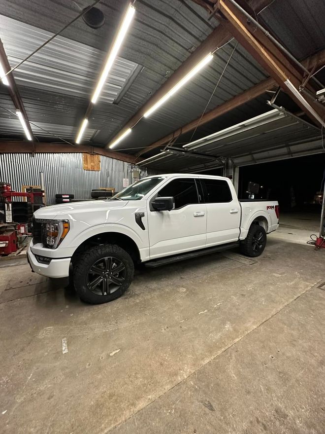 White pickup truck parked inside a garage. Black wheels, dark trim. Fluorescent lights above.
