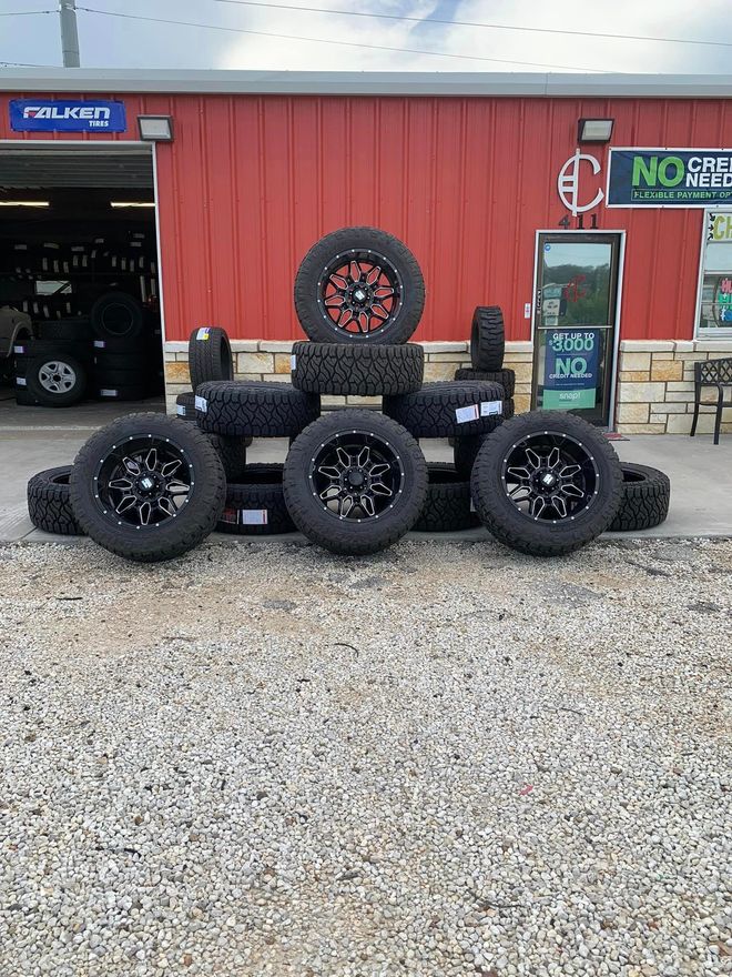 Tires and wheels displayed outside a tire shop with a red exterior. Black and red colors are prominent.