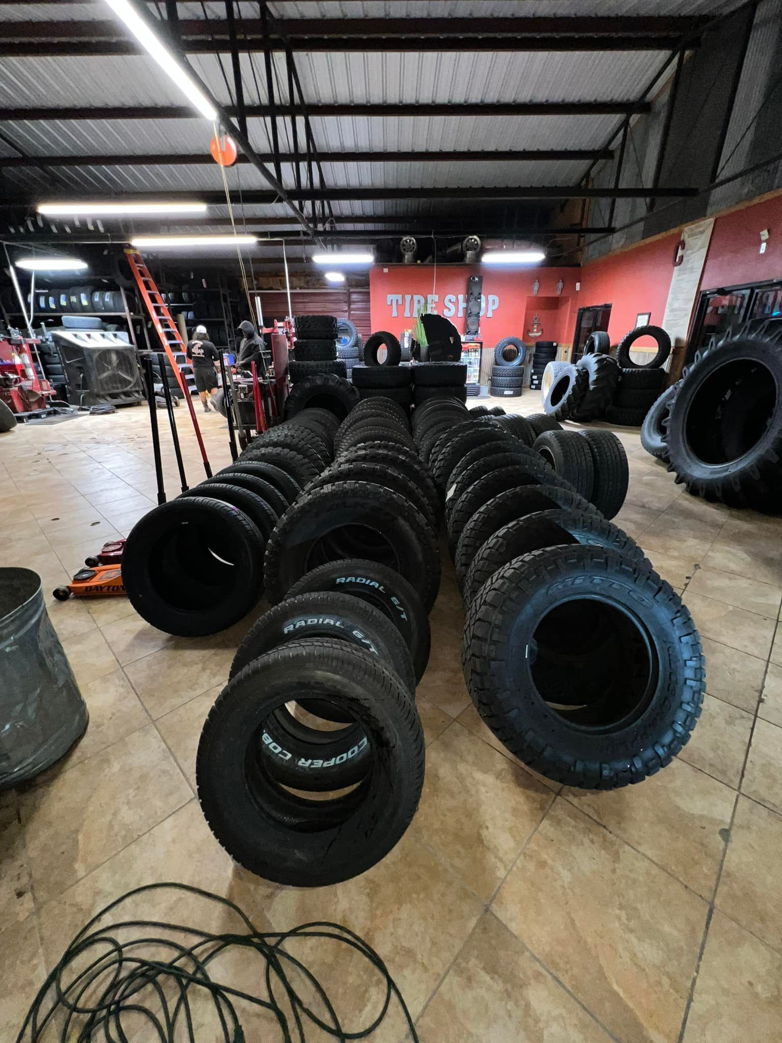 Rows of tires stacked in a shop. A ladder and tools are visible in the background, suggesting a tire store.