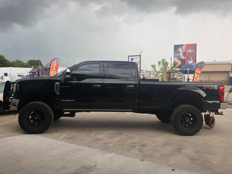 Black lifted Ford F-350 truck parked outside, dark tires, overcast sky.
